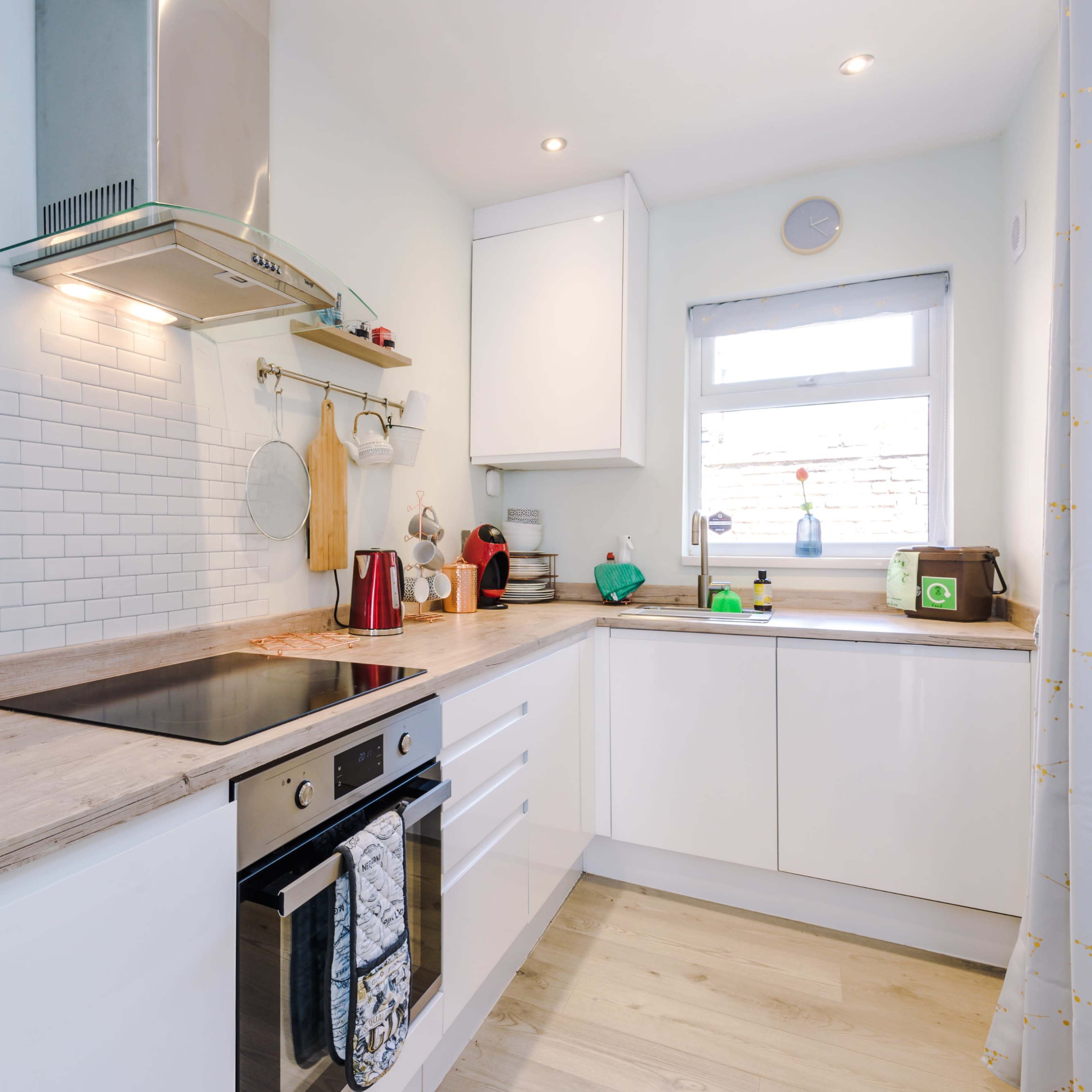 A modern kitchen with white cabinetry, a stainless steel range hood, and a wooden countertop, featuring appliances like a toaster and a kettle.