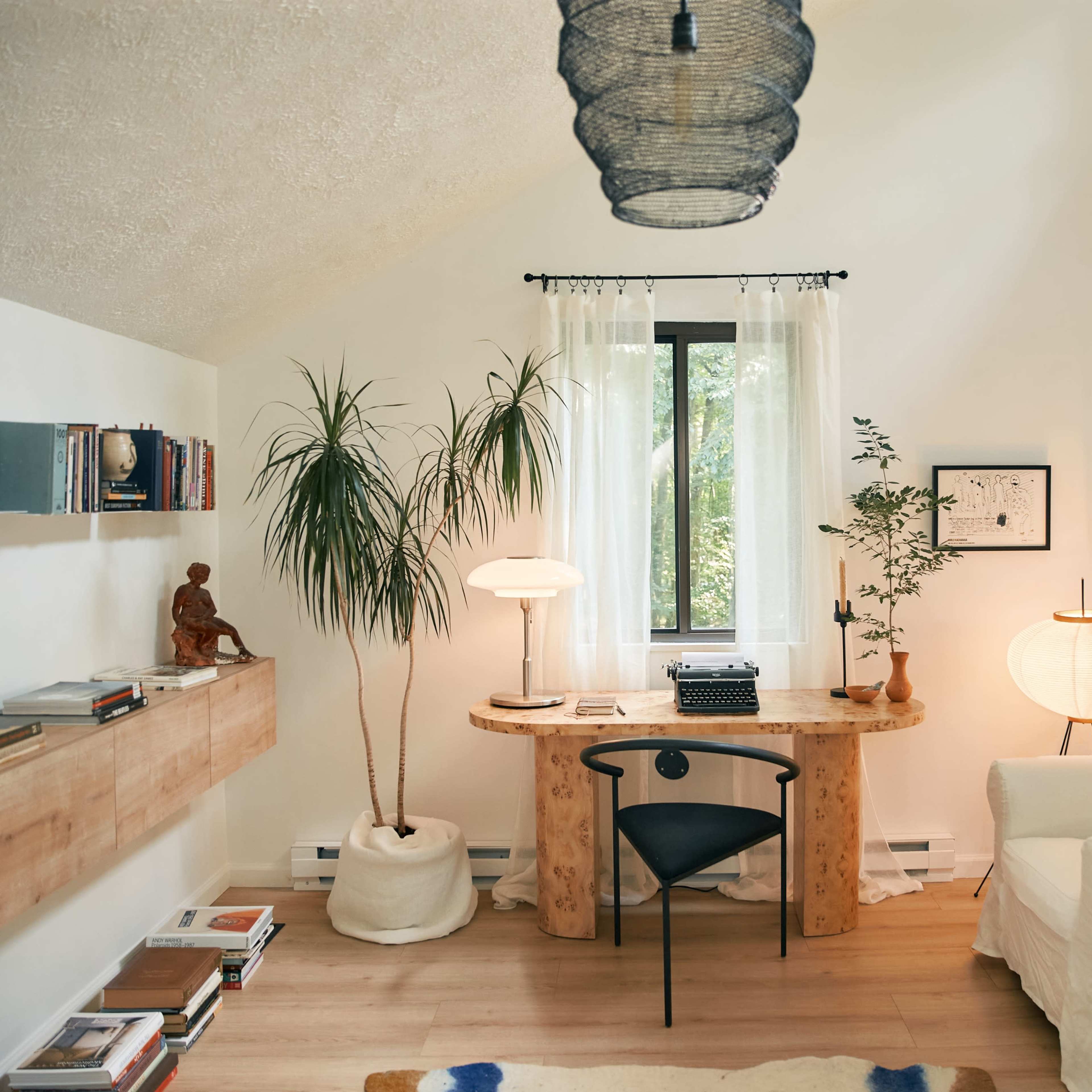 A minimalist home office with a wooden desk, a typewriter, a chair, plants, and soft lighting.
