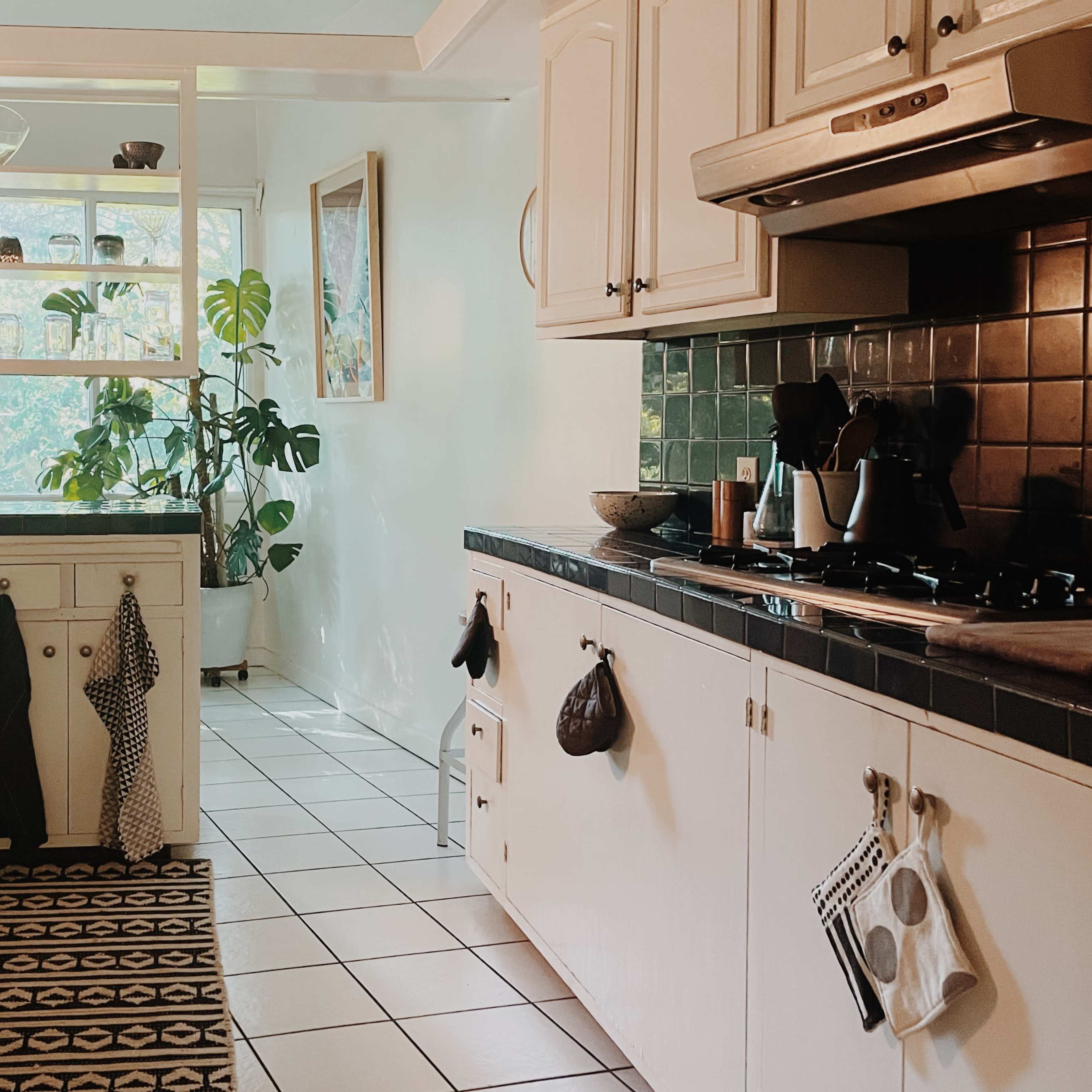 A well-organized kitchen with white cabinetry, a green tiled backsplash, and a large window providing natural light.