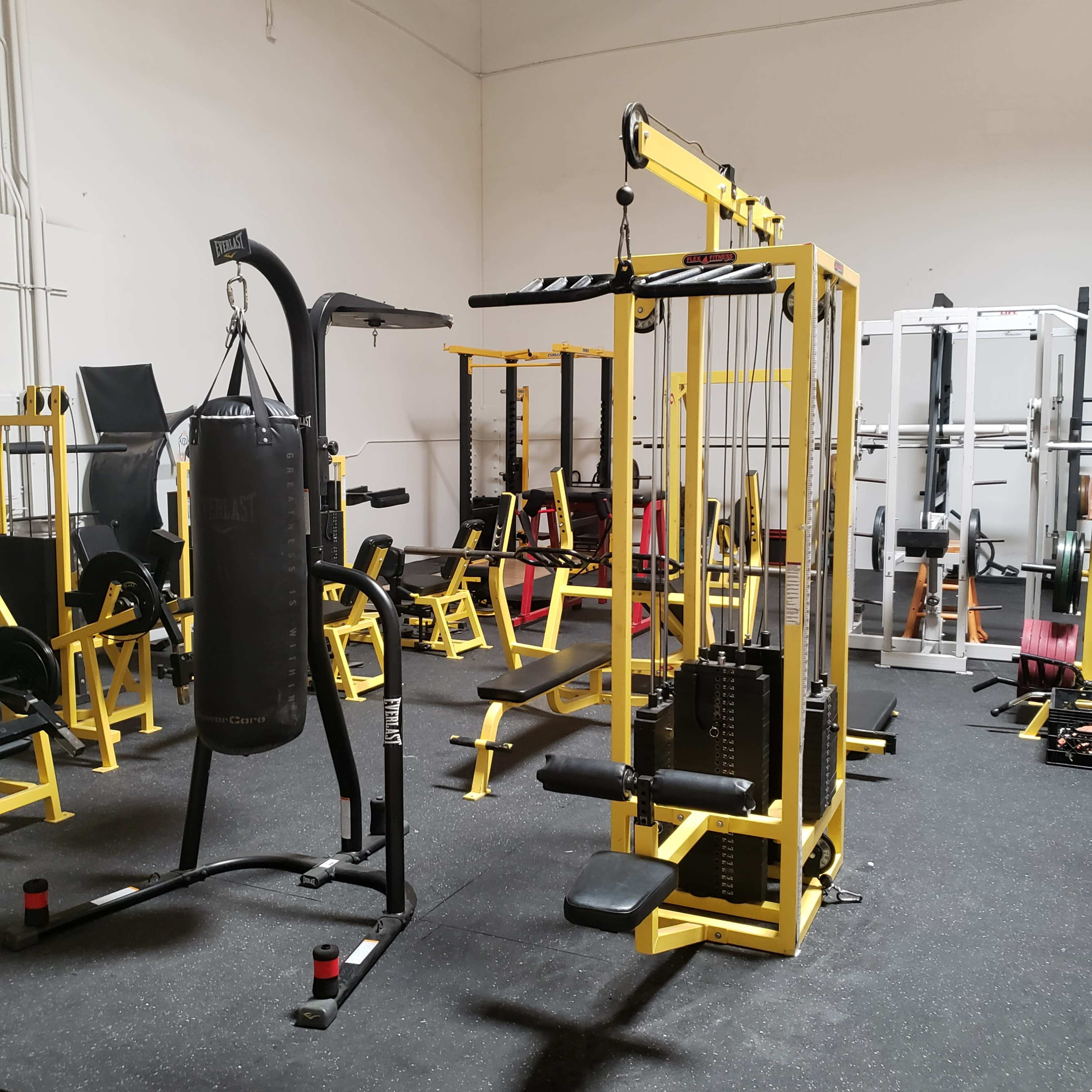 A gym interior featuring various workout equipment, including a cable machine, a punching bag, and weightlifting stations, all arranged on a rubberized floor.