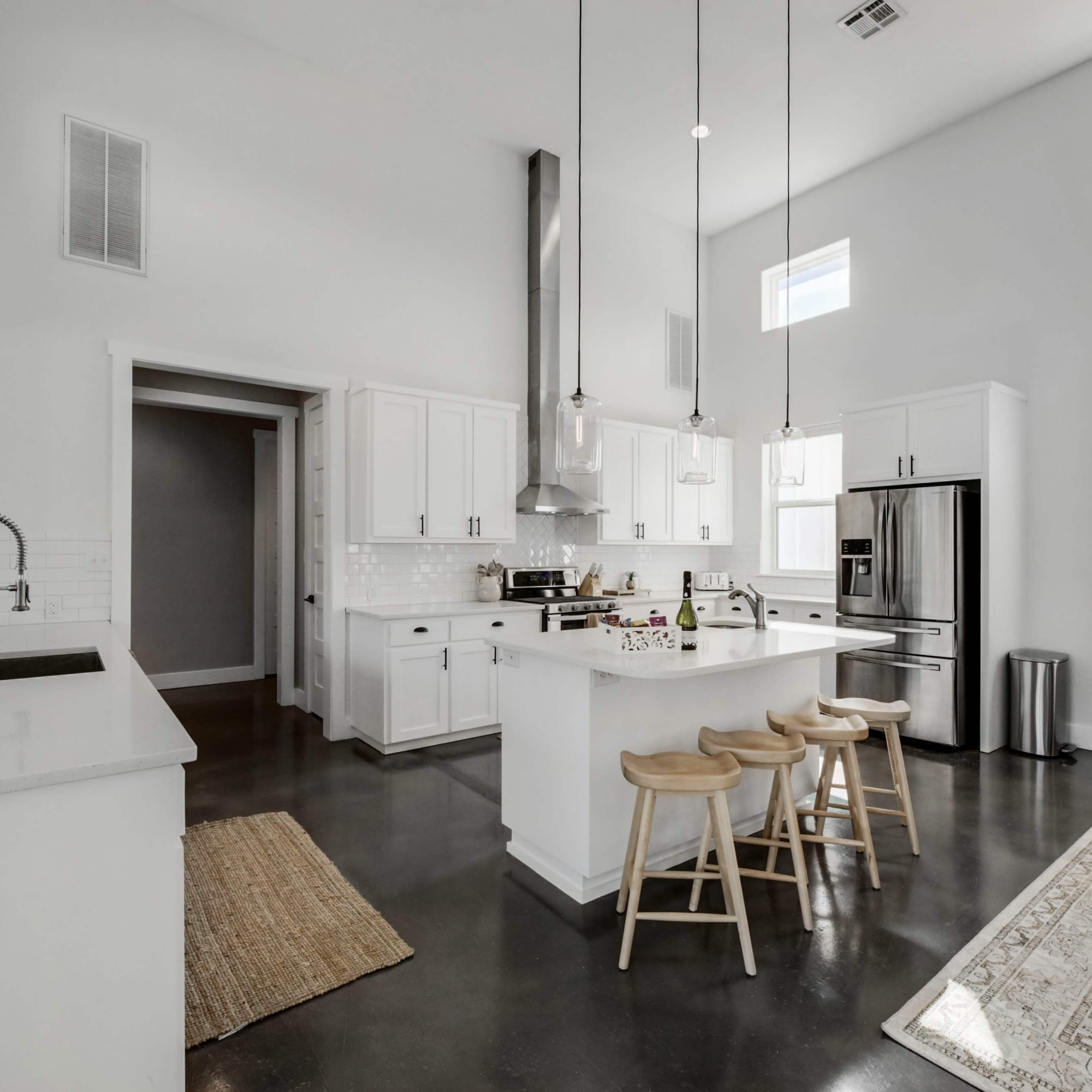 A modern kitchen featuring white cabinetry, stainless steel appliances, and a central island with three wooden stools.