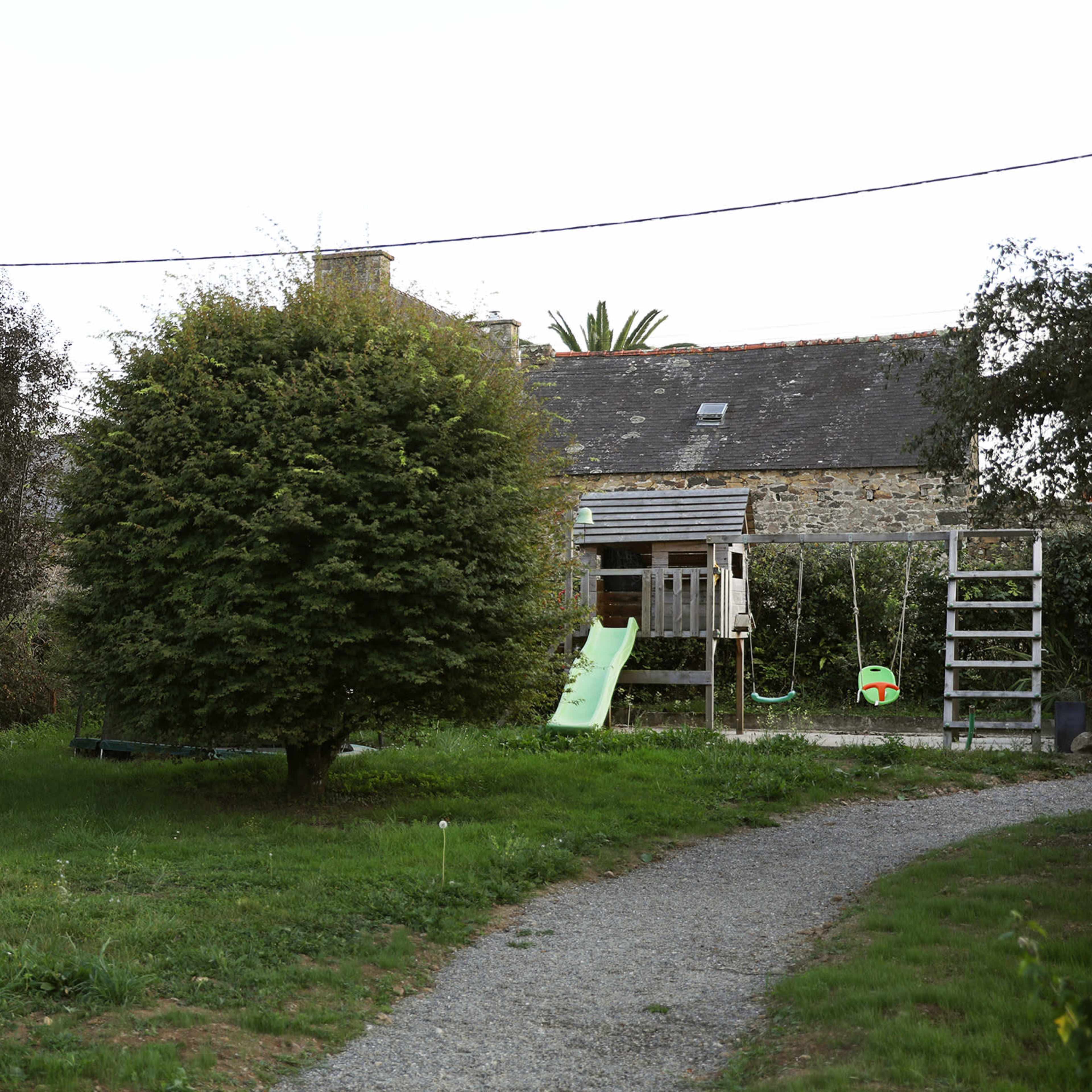 The scene shows a grassy area with a tree and a play structure, surrounded by low buildings and a gravel pathway.
