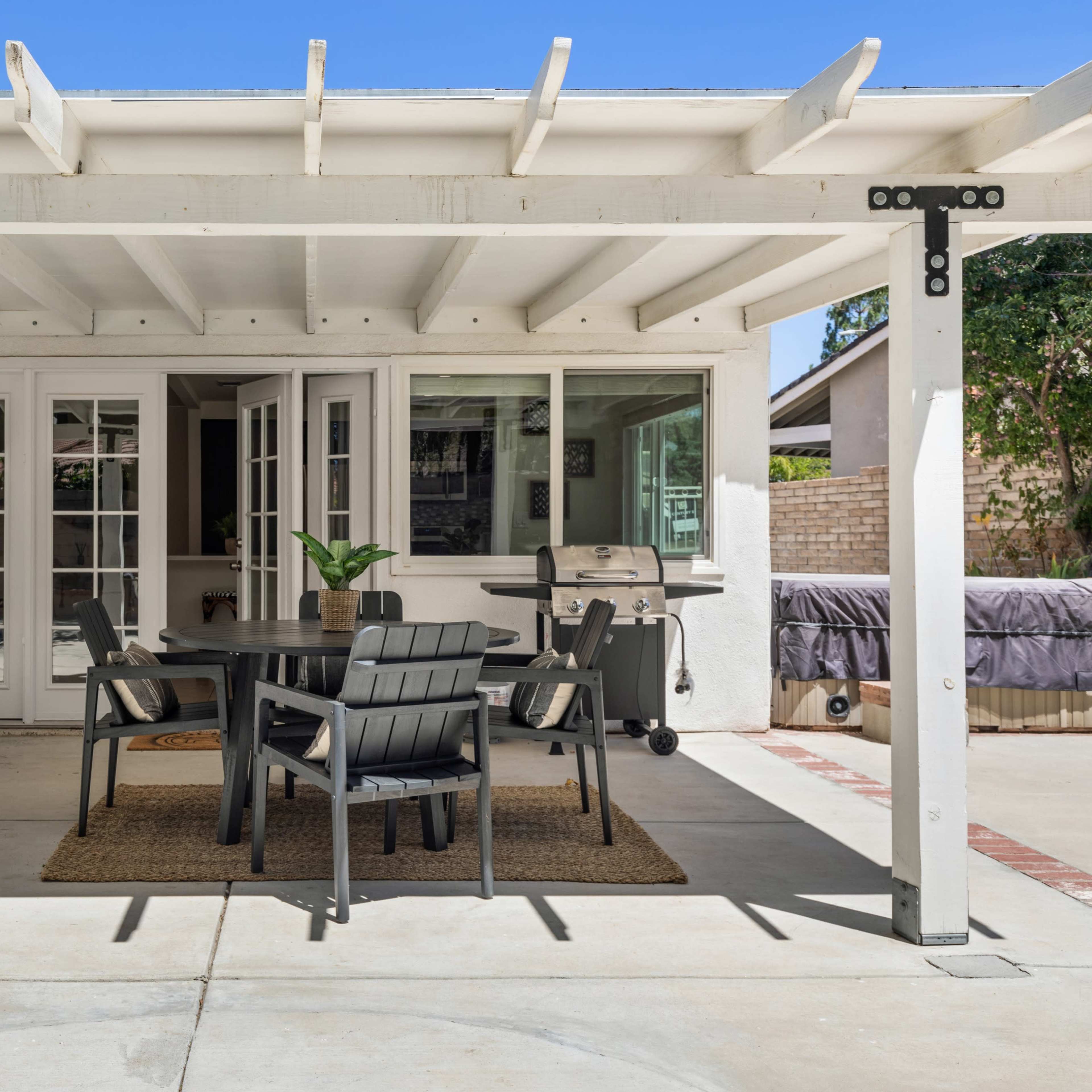 A covered outdoor patio with a table and chairs, a grill, and large French doors leading into a house.