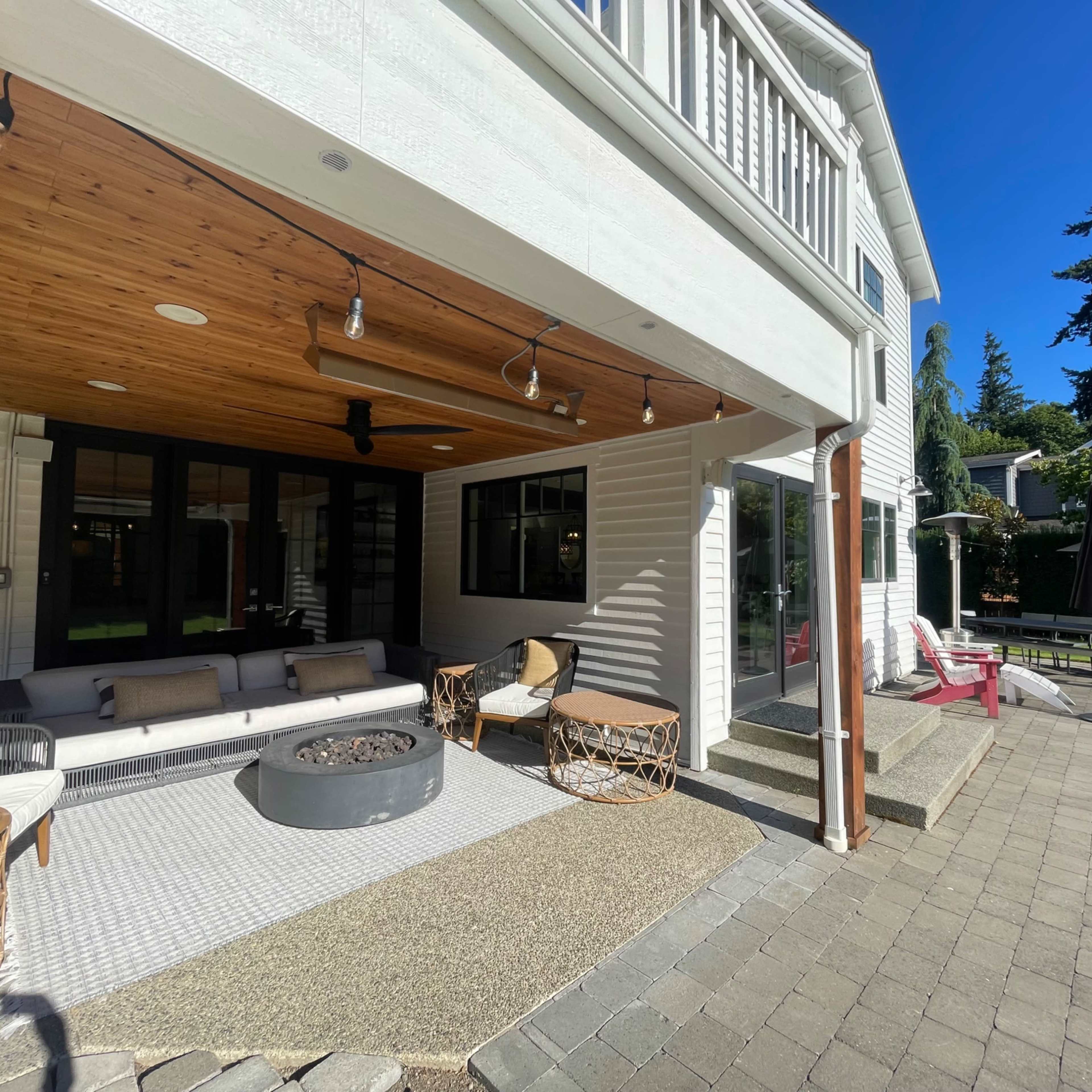 A modern outdoor living space featuring a covered seating area with a fire pit and a stone patio at the entrance to a house.