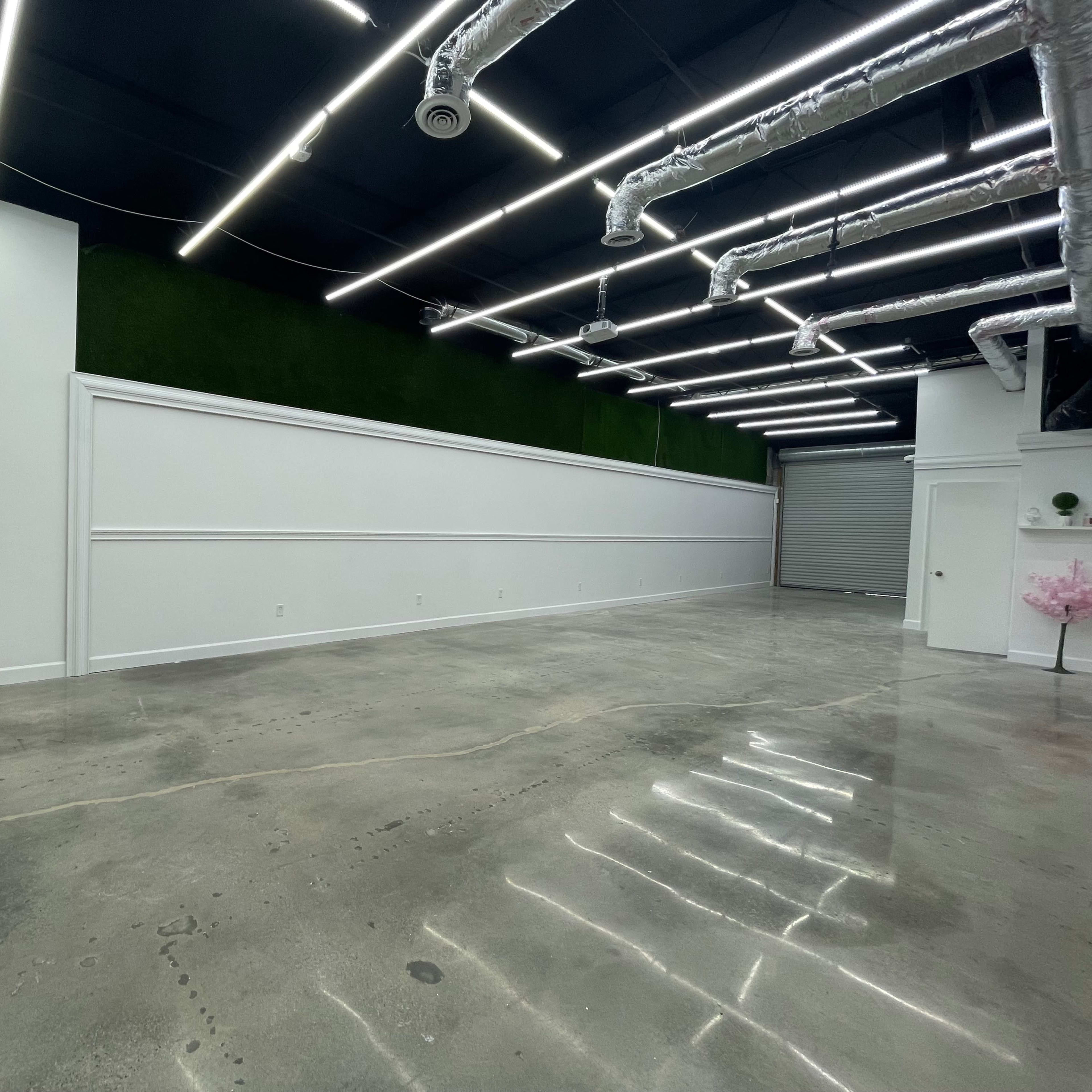 An empty commercial space with polished concrete floors, bright overhead lighting, and a green accent wall.