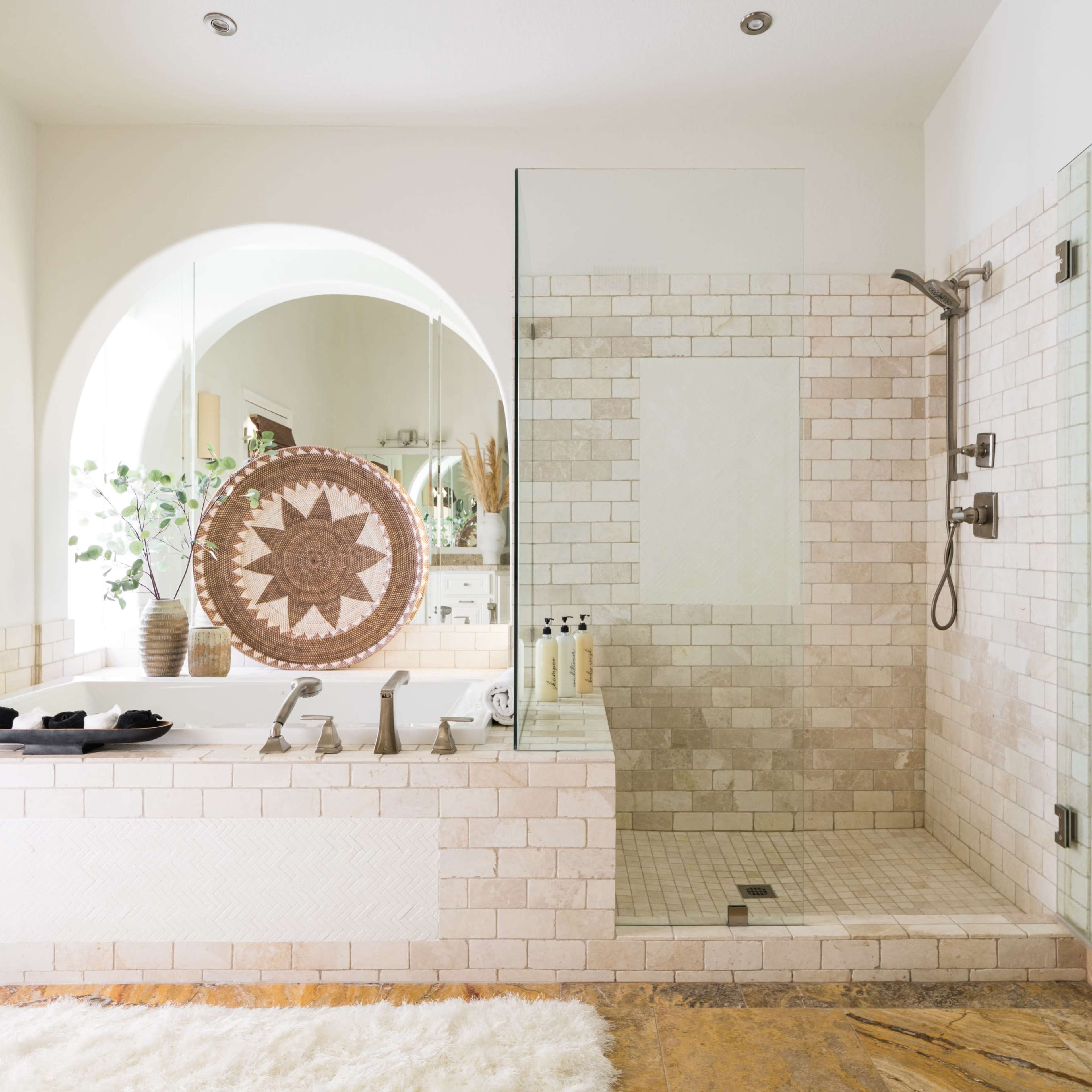 A spacious bathroom featuring a shower area with glass walls, a freestanding tub, and tile walls in neutral tones.