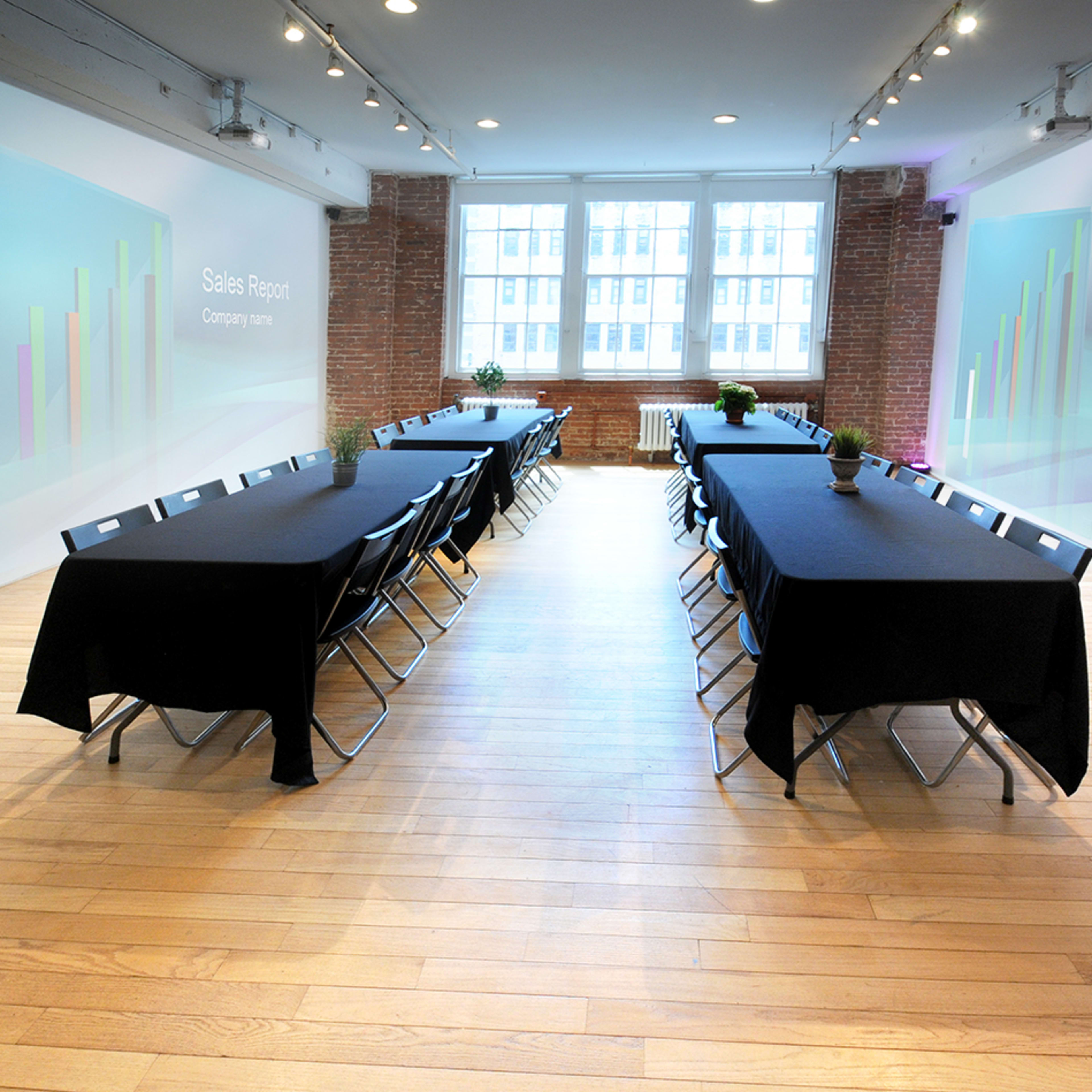 A conference room with two rows of tables set up for a meeting, featuring digital screens displaying "Sales Report" on the walls.