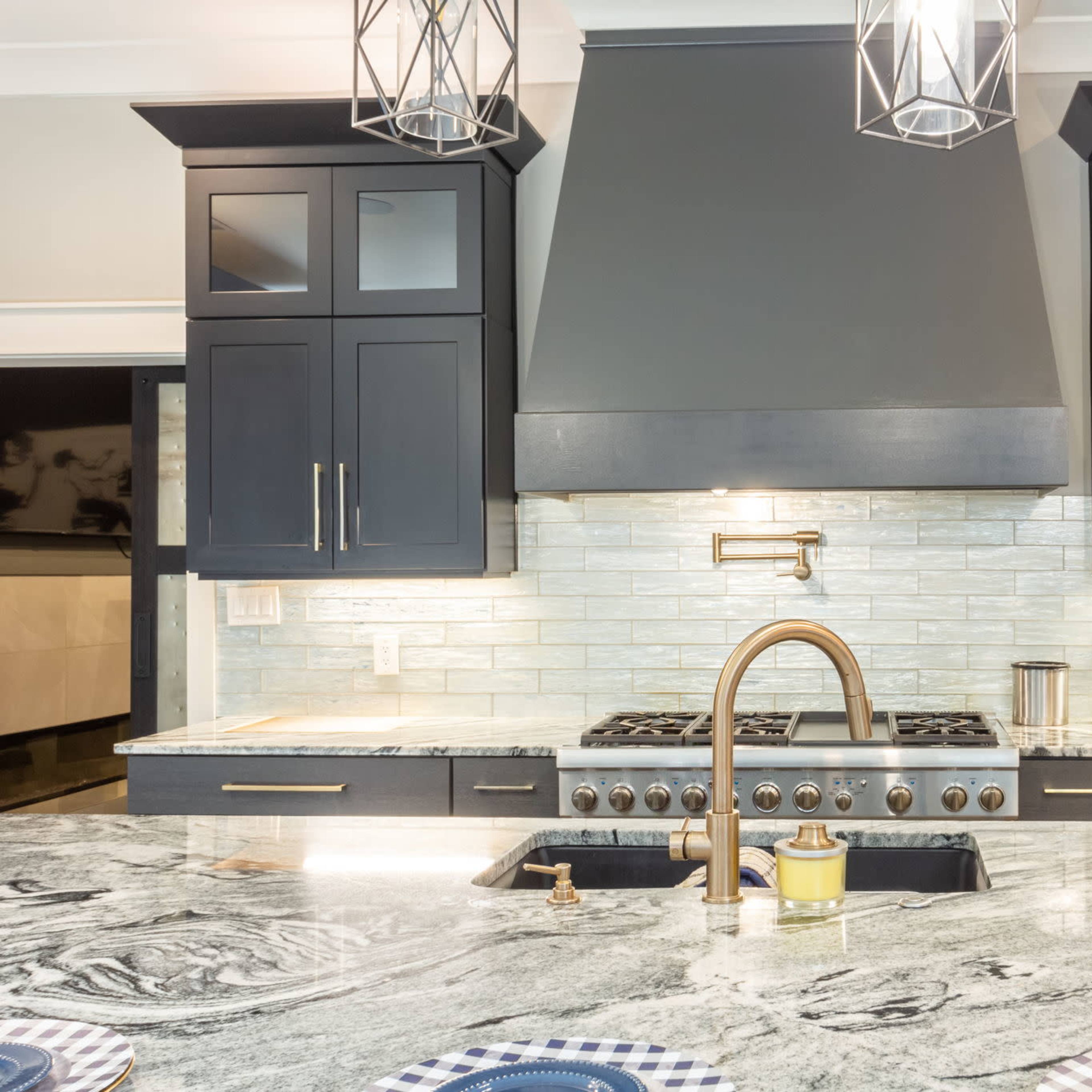 A modern kitchen featuring dark cabinetry, a stainless steel gas stove, and a large granite countertop with a farmhouse sink.