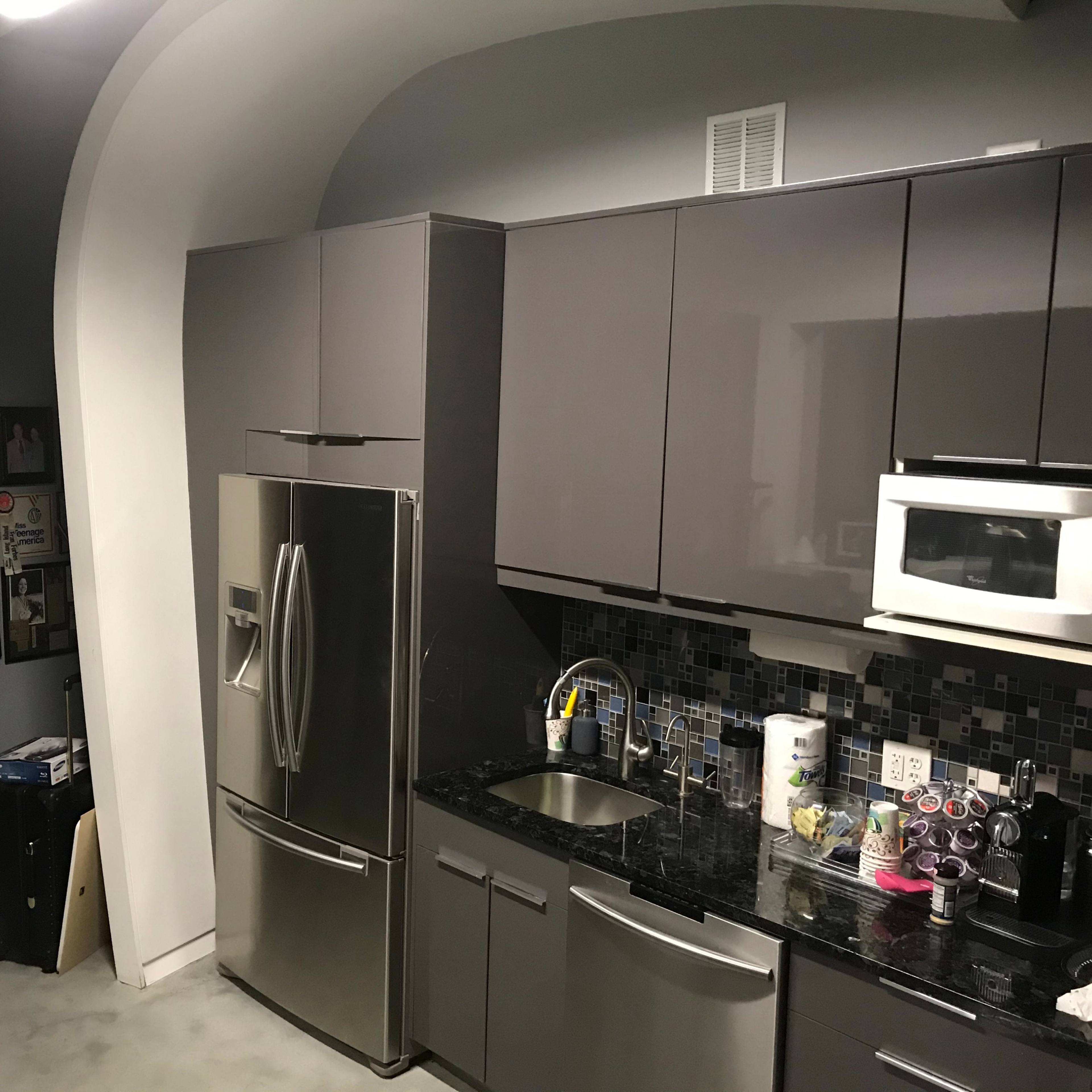 A modern kitchen features stainless steel appliances, dark cabinetry, and a mosaic tile backsplash.
