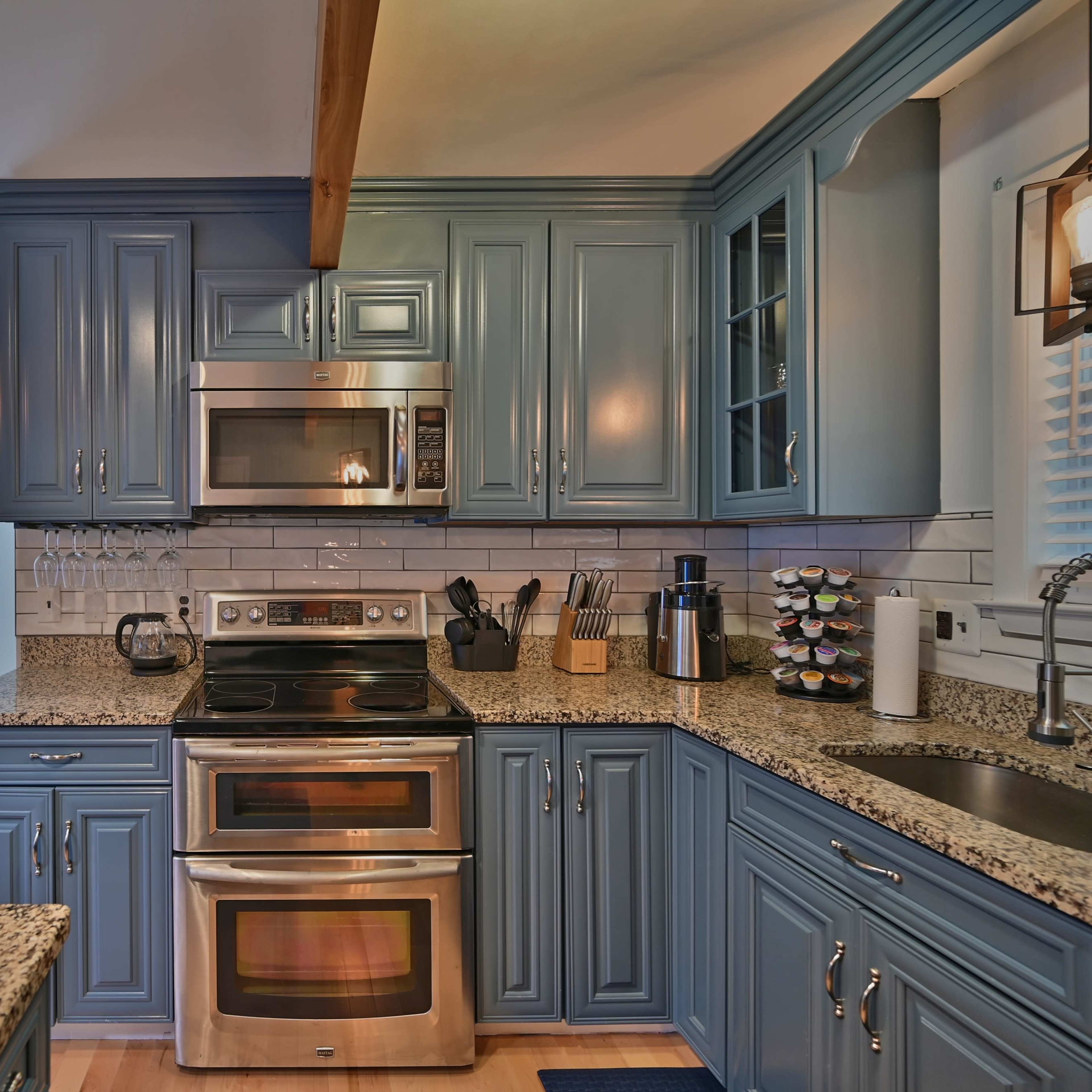 A modern kitchen featuring blue cabinets, a stainless steel oven and microwave, and a granite countertop.