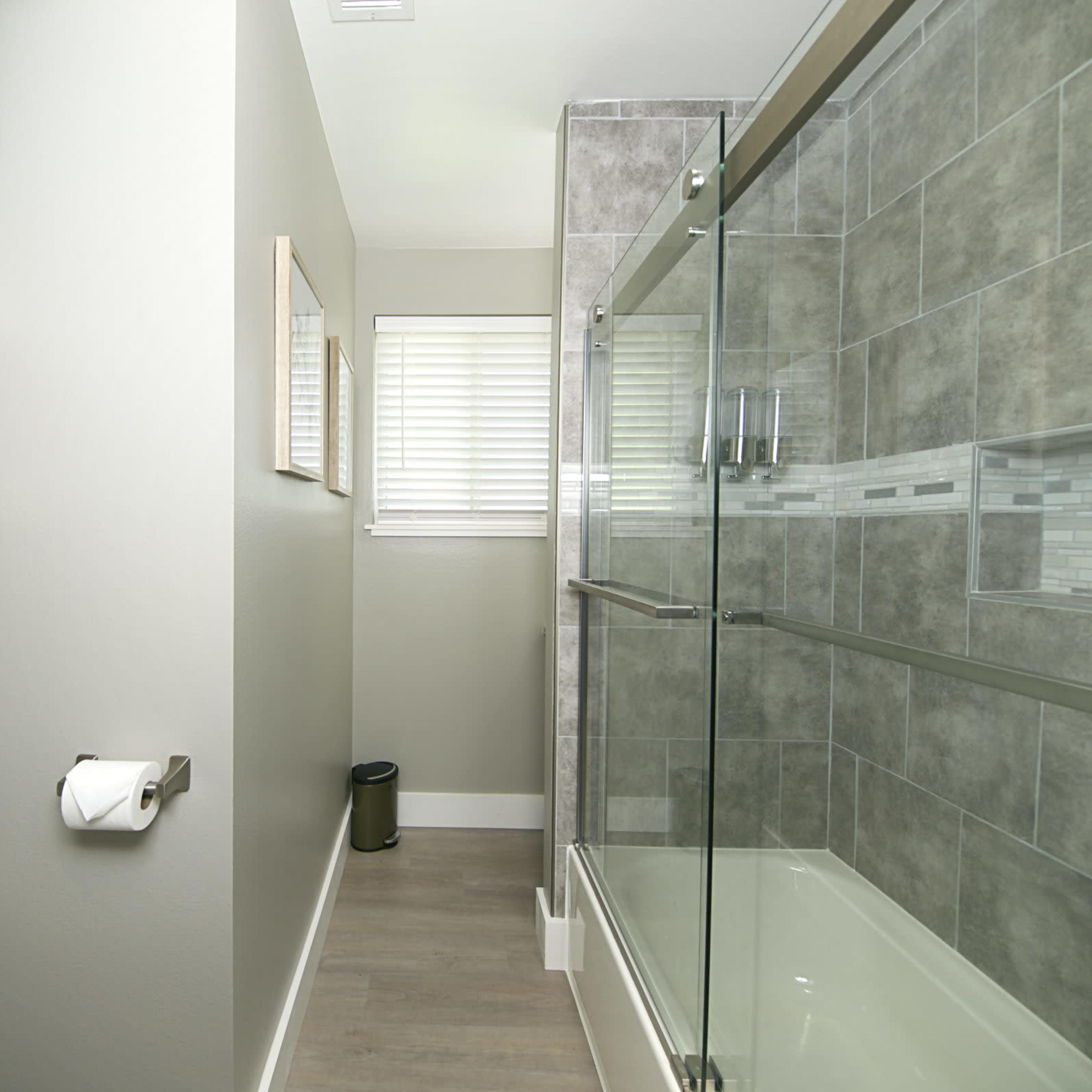 A modern bathroom featuring a glass shower enclosure, a toilet, and neatly arranged towels on a shelf.
