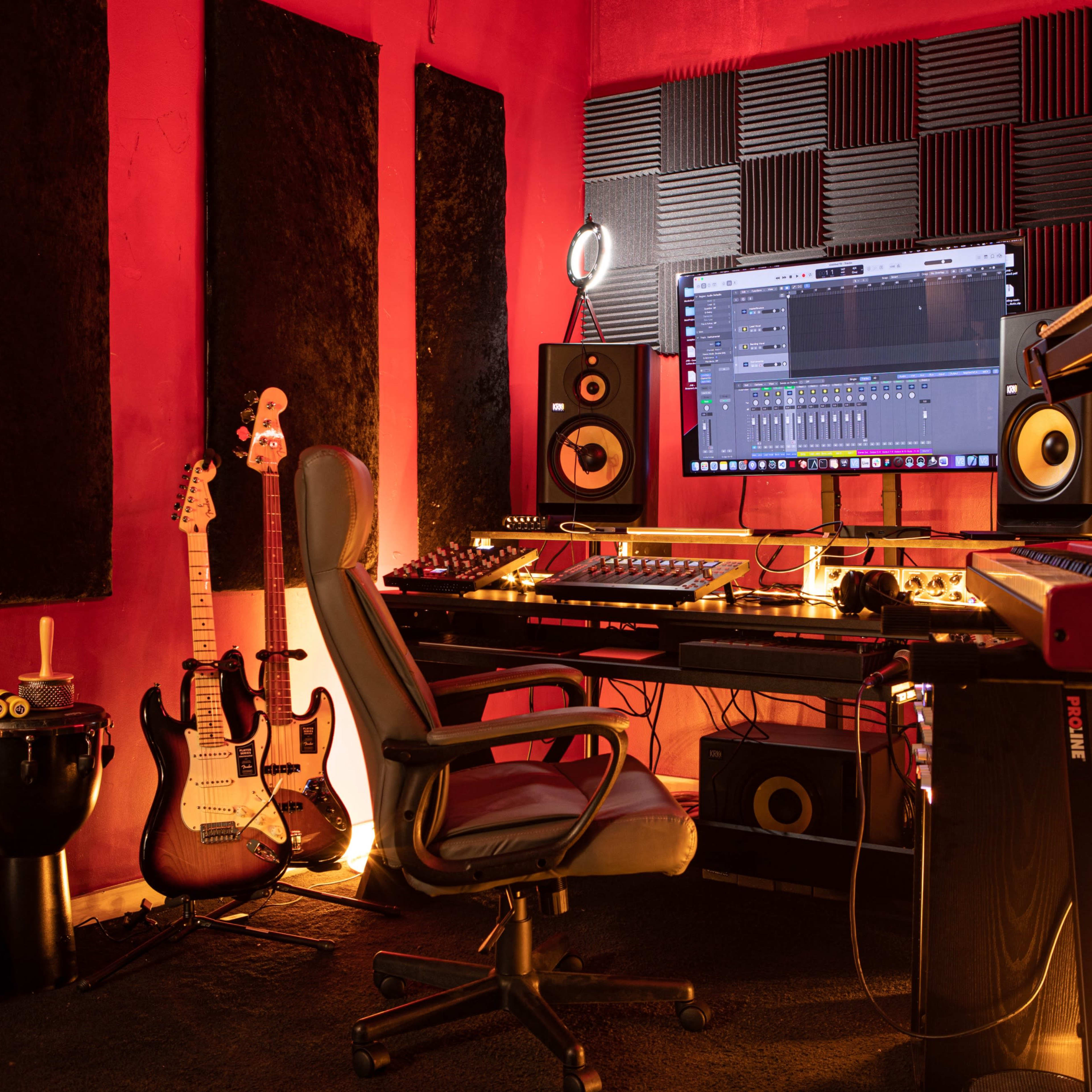 A music production studio with a large monitor, various musical instruments, a chair, and soundproof panels on the walls.