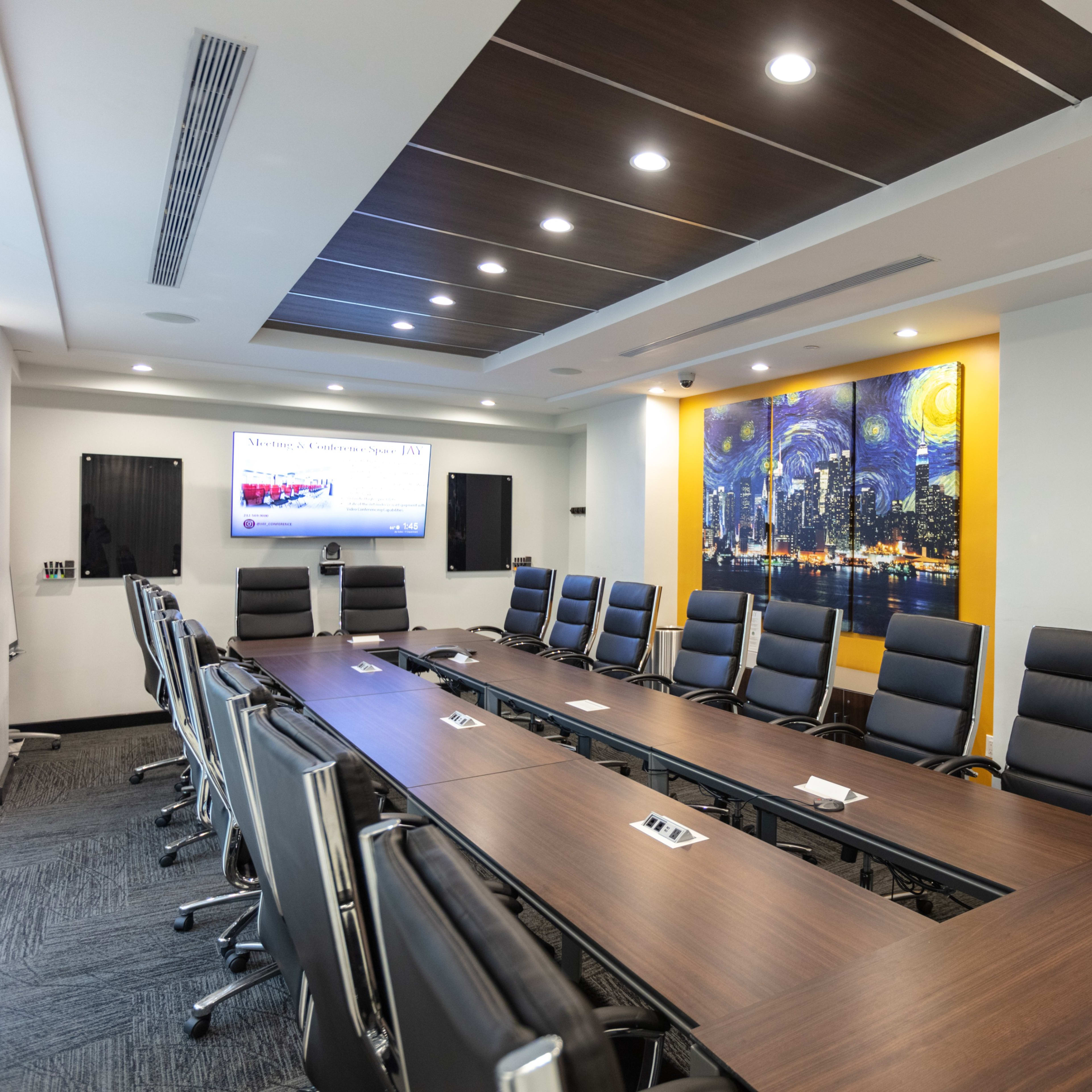 A modern conference room with a large wooden table surrounded by black office chairs and a wall featuring a cityscape mural.