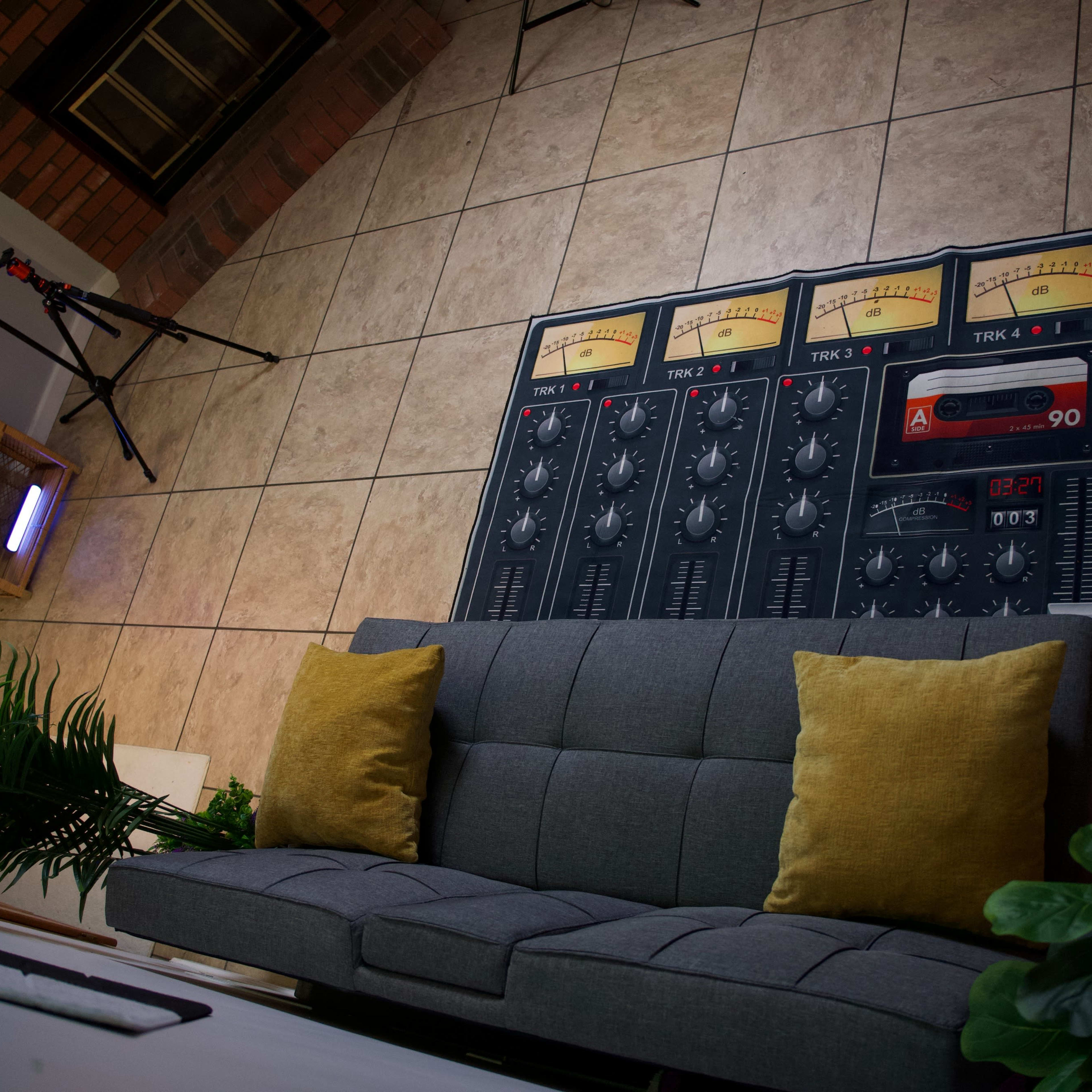 A living room with tiled flooring, featuring a gray sofa with yellow cushions and a large mural of a four-track audio mixer on the wall behind it.