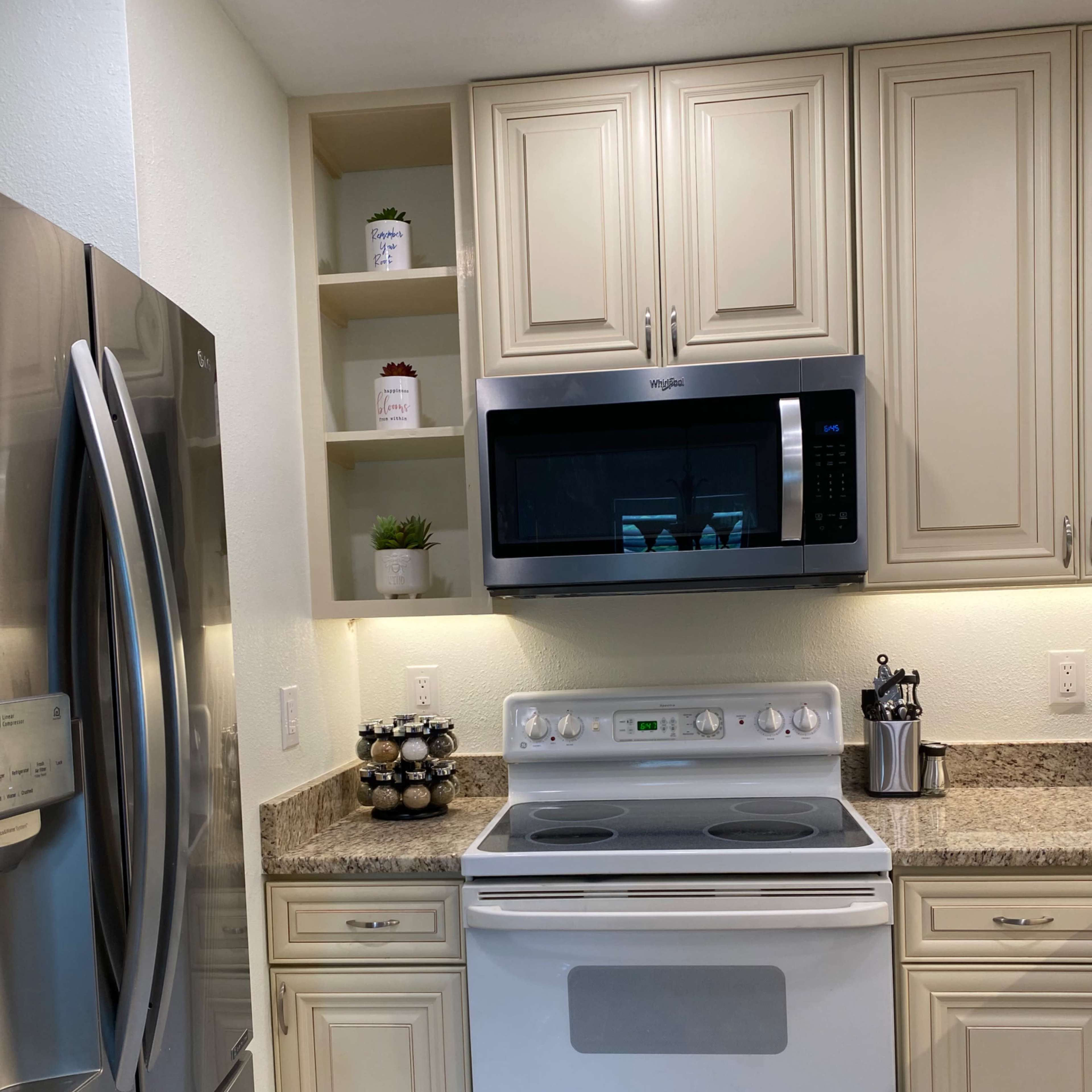 A kitchen features a white stove and microwave above it, with beige cabinets and granite countertops, alongside a stainless steel refrigerator.