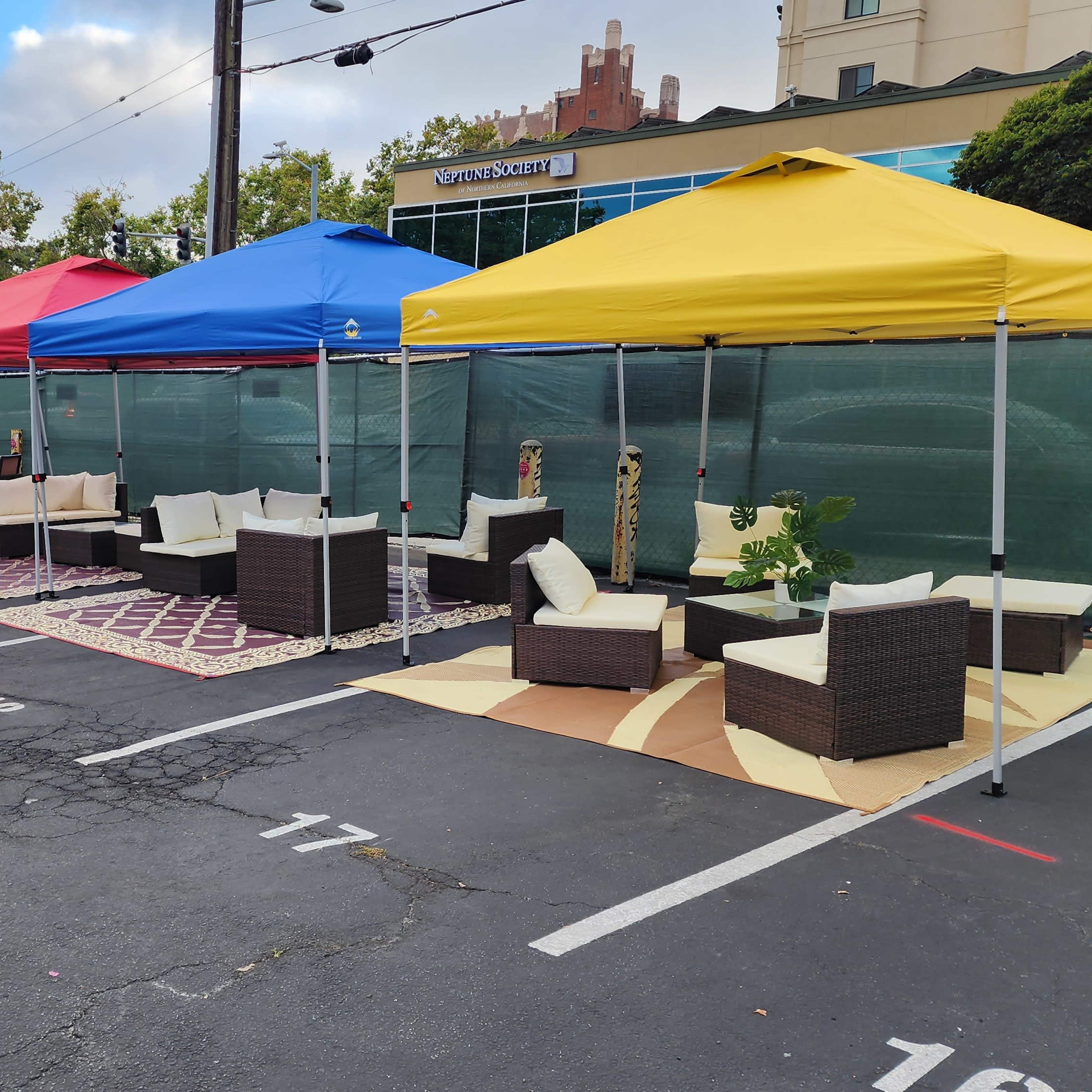 Several outdoor seating arrangements under colored canopies in a parking lot.