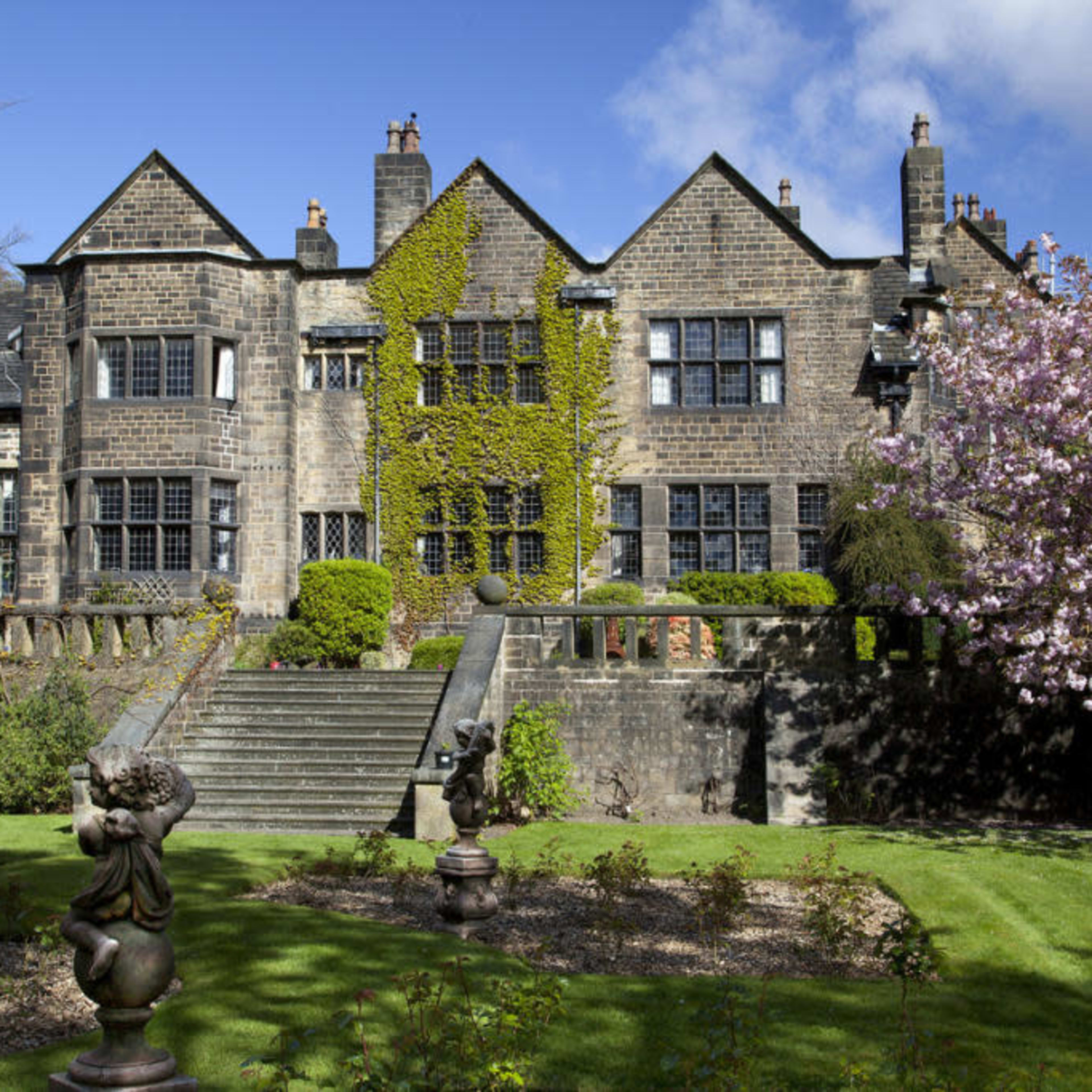 A large stone house with ivy climbing its walls, surrounded by well-maintained gardens and trees.