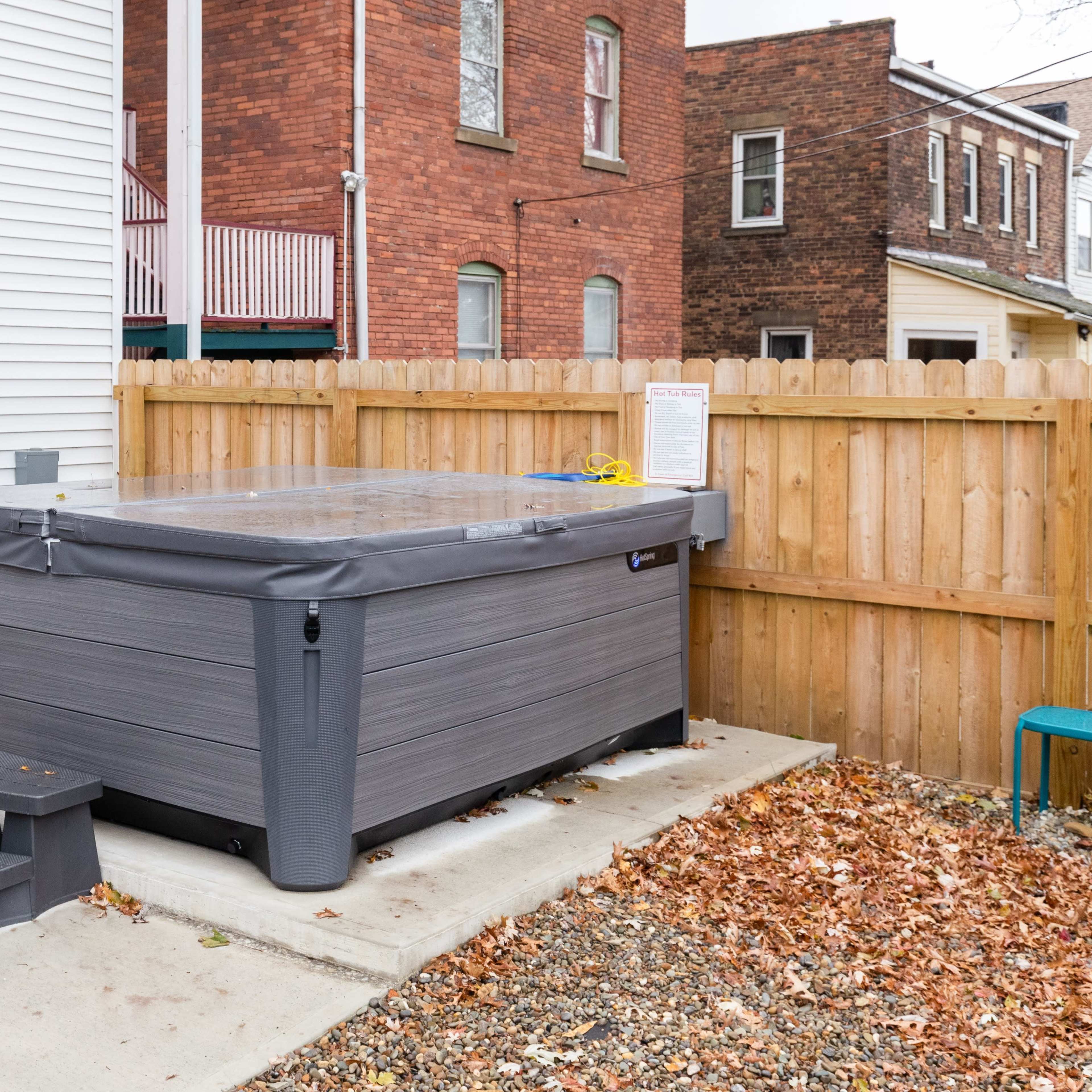 A hot tub located on a stony surface beside a house, enclosed by a wooden fence.