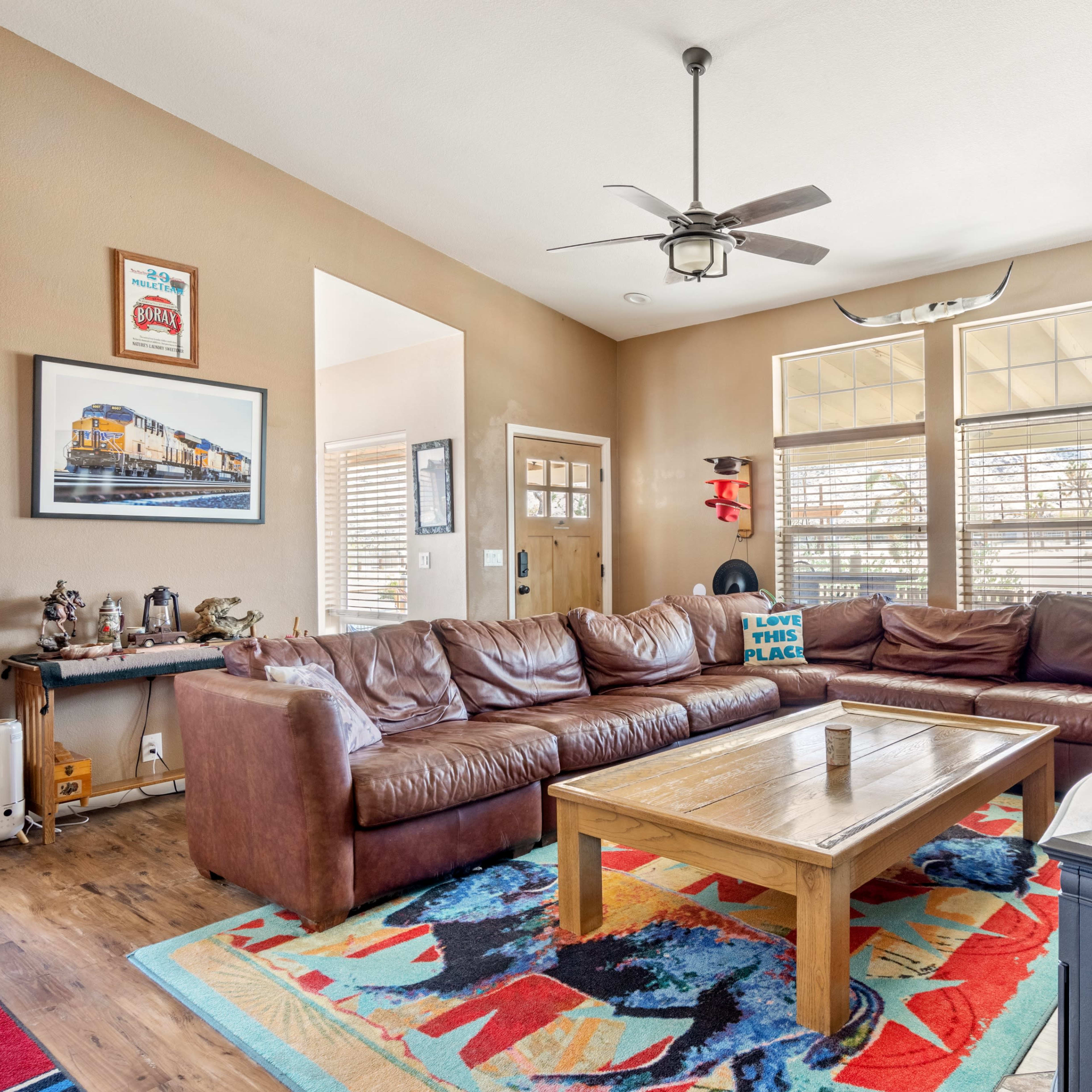 A living room with a large brown leather sectional sofa, a wooden coffee table, and colorful area rugs on the floor.