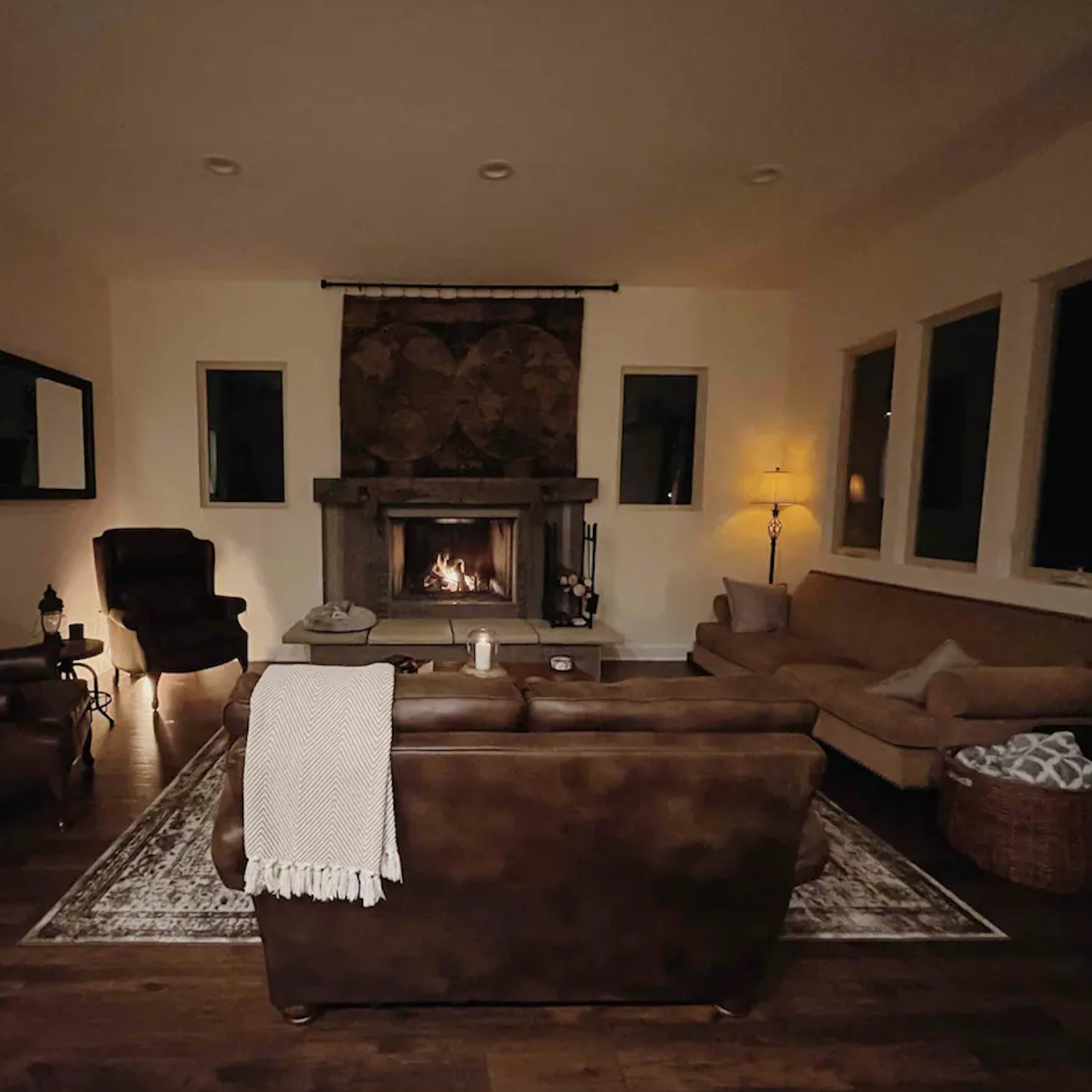 A cozy living room features a stone fireplace, two armchairs, a couch, and a coffee table, all arranged on wooden flooring.