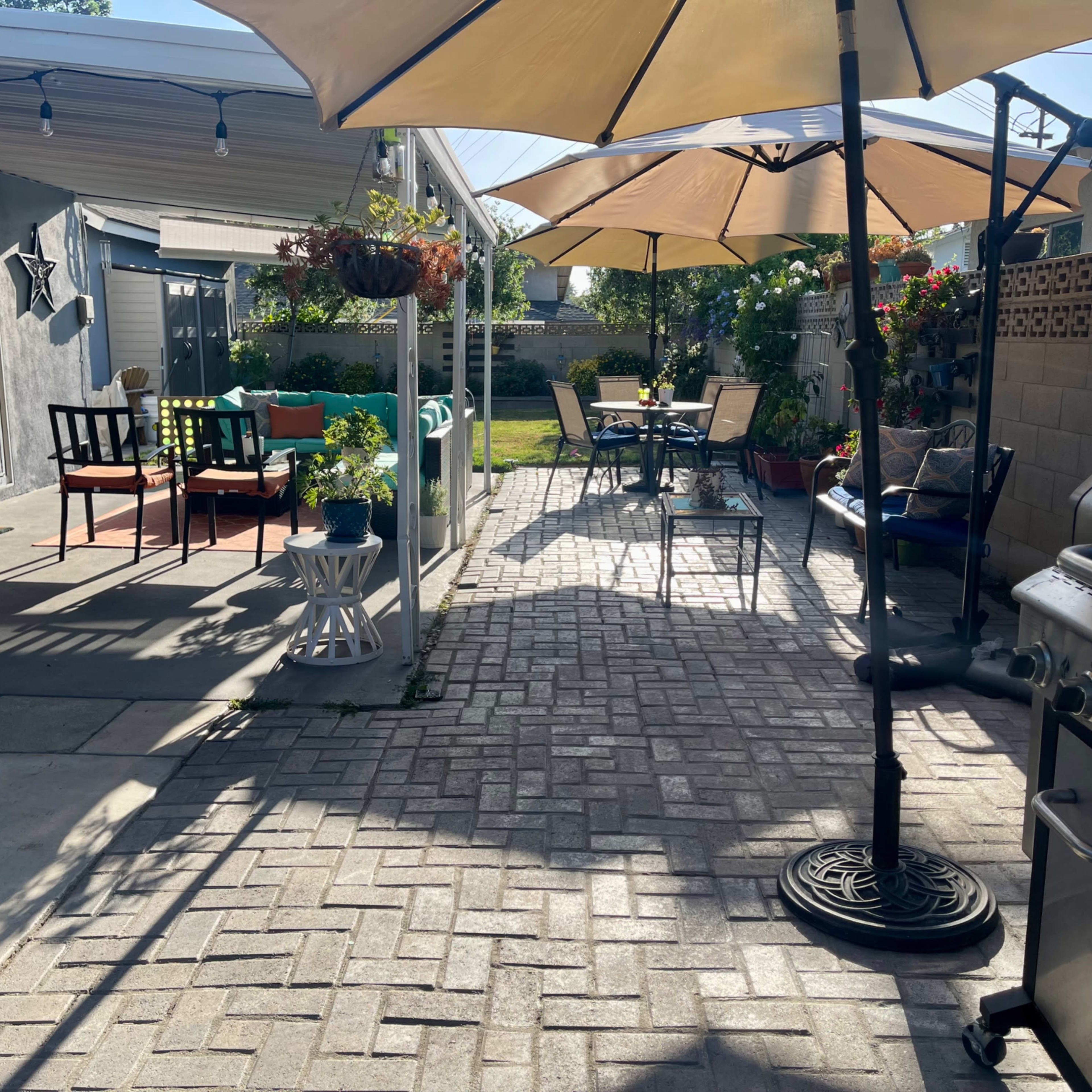 A patio area with outdoor furniture, two large umbrellas, potted plants, and a grill.