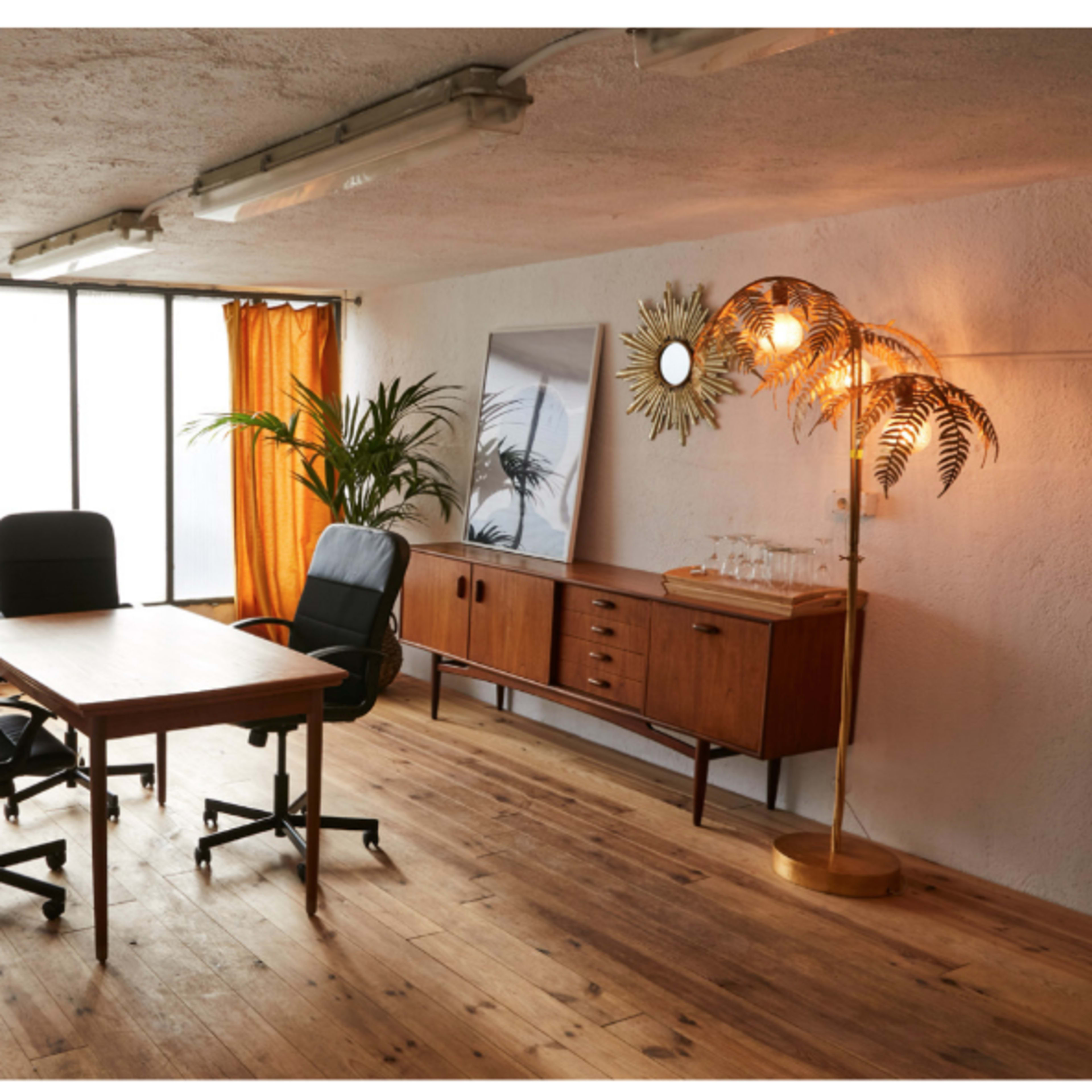 A spacious room features a wooden table, two office chairs, a cabinet, and large windows with orange curtains.