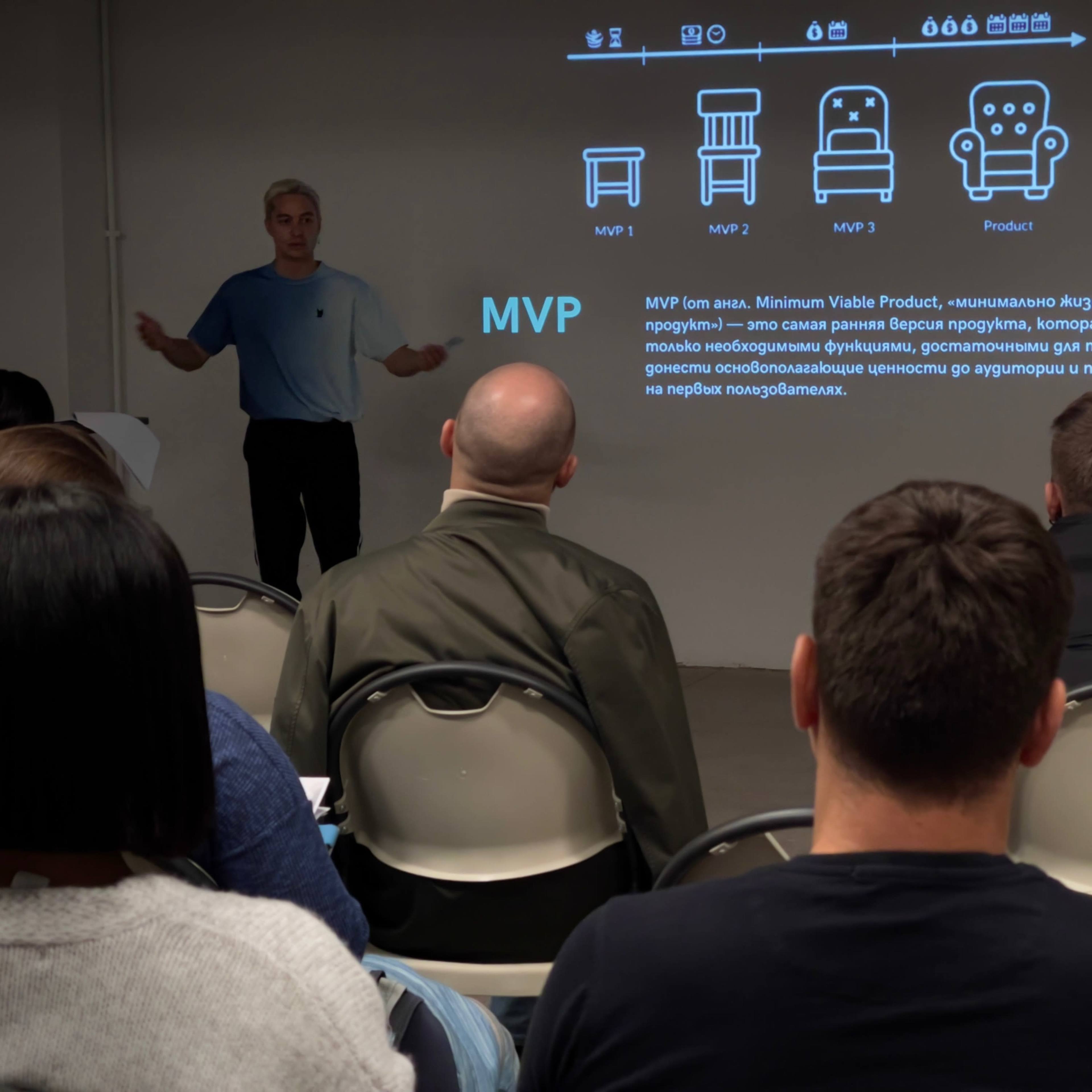 A speaker presents information about the Minimum Viable Product (MVP) in front of an audience seated in a small conference room.