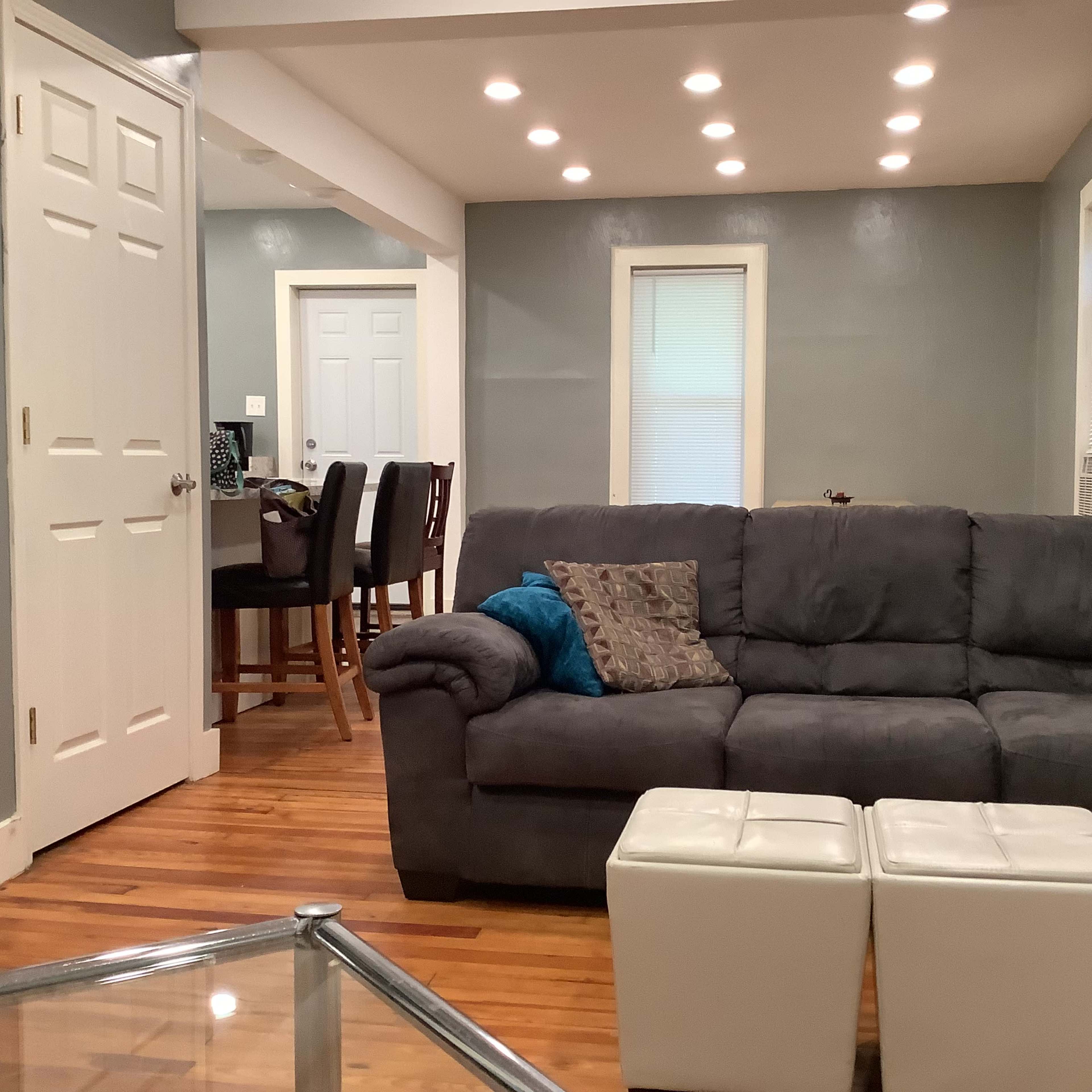 A living room with a gray couch, a glass coffee table, and a view of a dining area in the background.