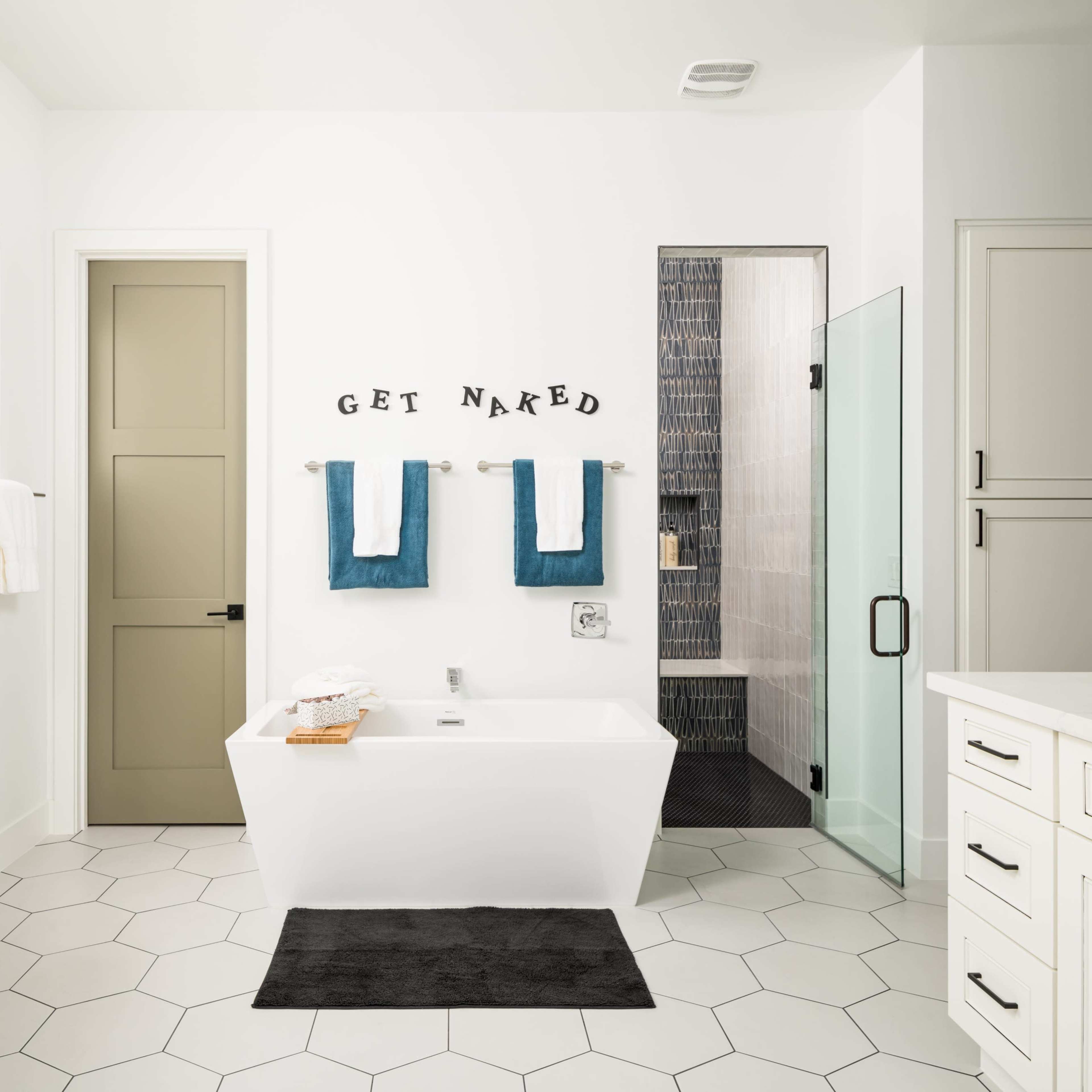 A modern bathroom with a freestanding bathtub, two white towels hanging on blue towel bars, and a glass shower enclosure, all set against a white backdrop with hexagonal floor tiles.