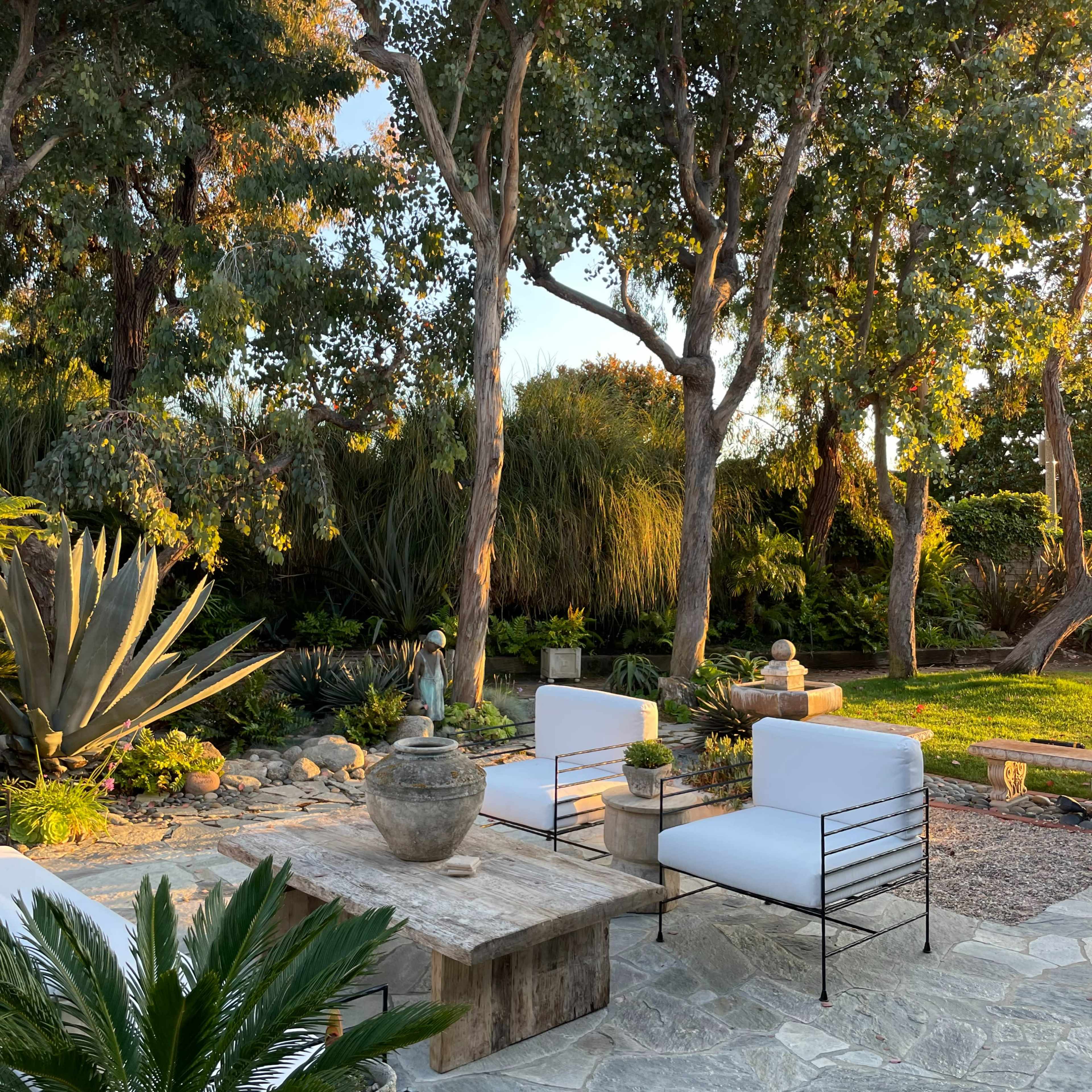 A landscaped outdoor area with stone seating, potted plants, and surrounded by tall trees.