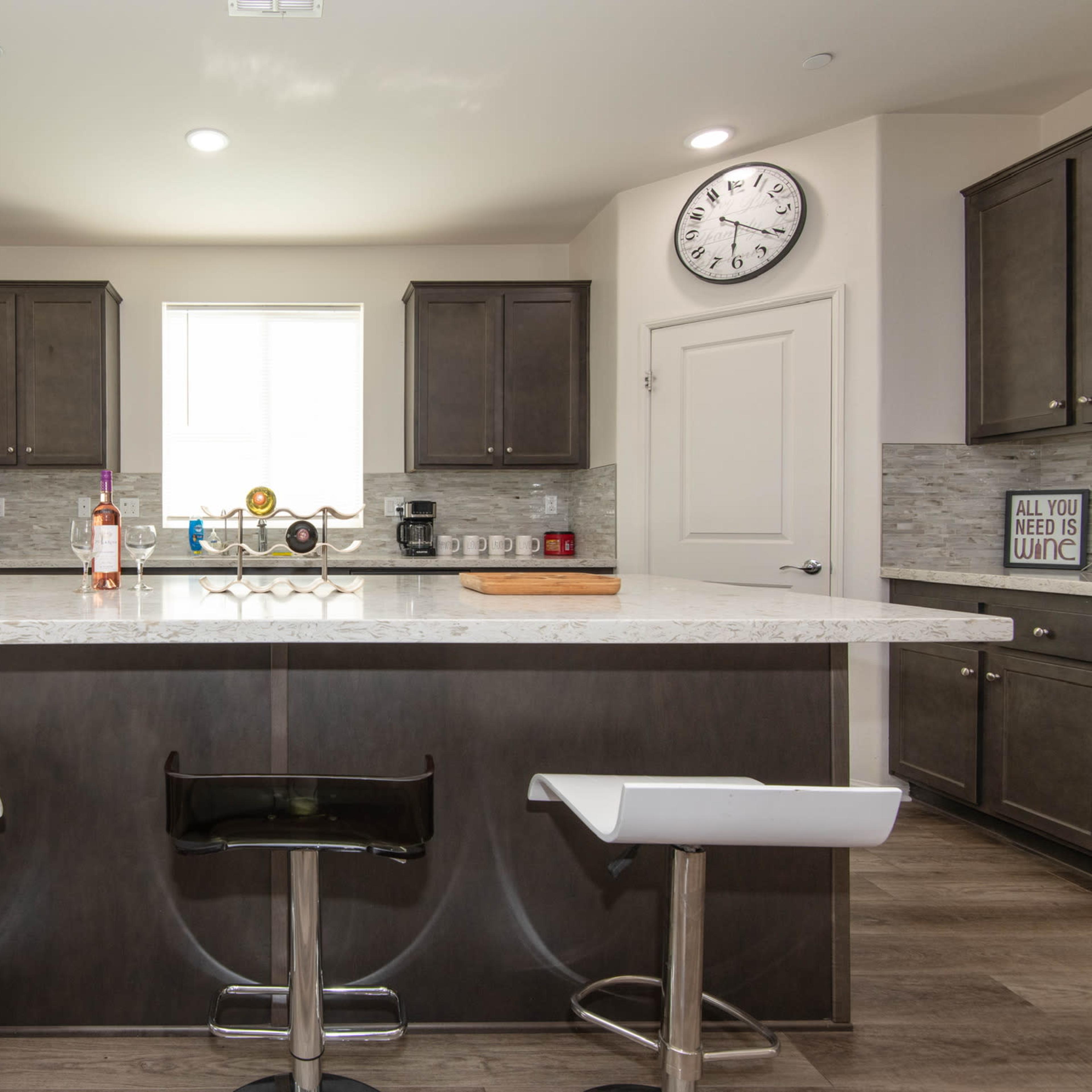 The kitchen features dark cabinetry, a large marble island with bar stools, and stainless steel appliances.