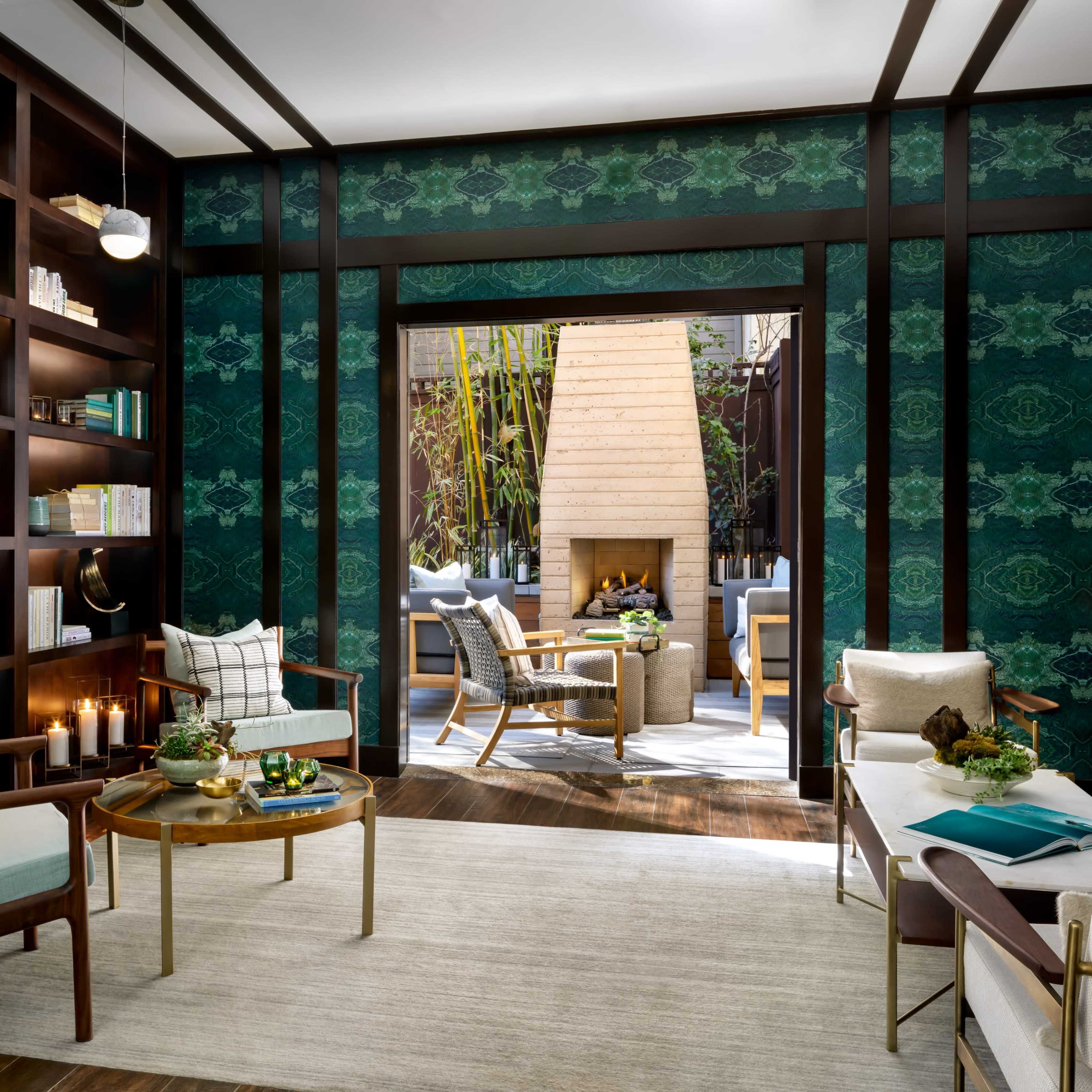 A modern library area features a built-in bookshelf filled with books, a cozy seating arrangement, and a view of an outdoor space with a fireplace.