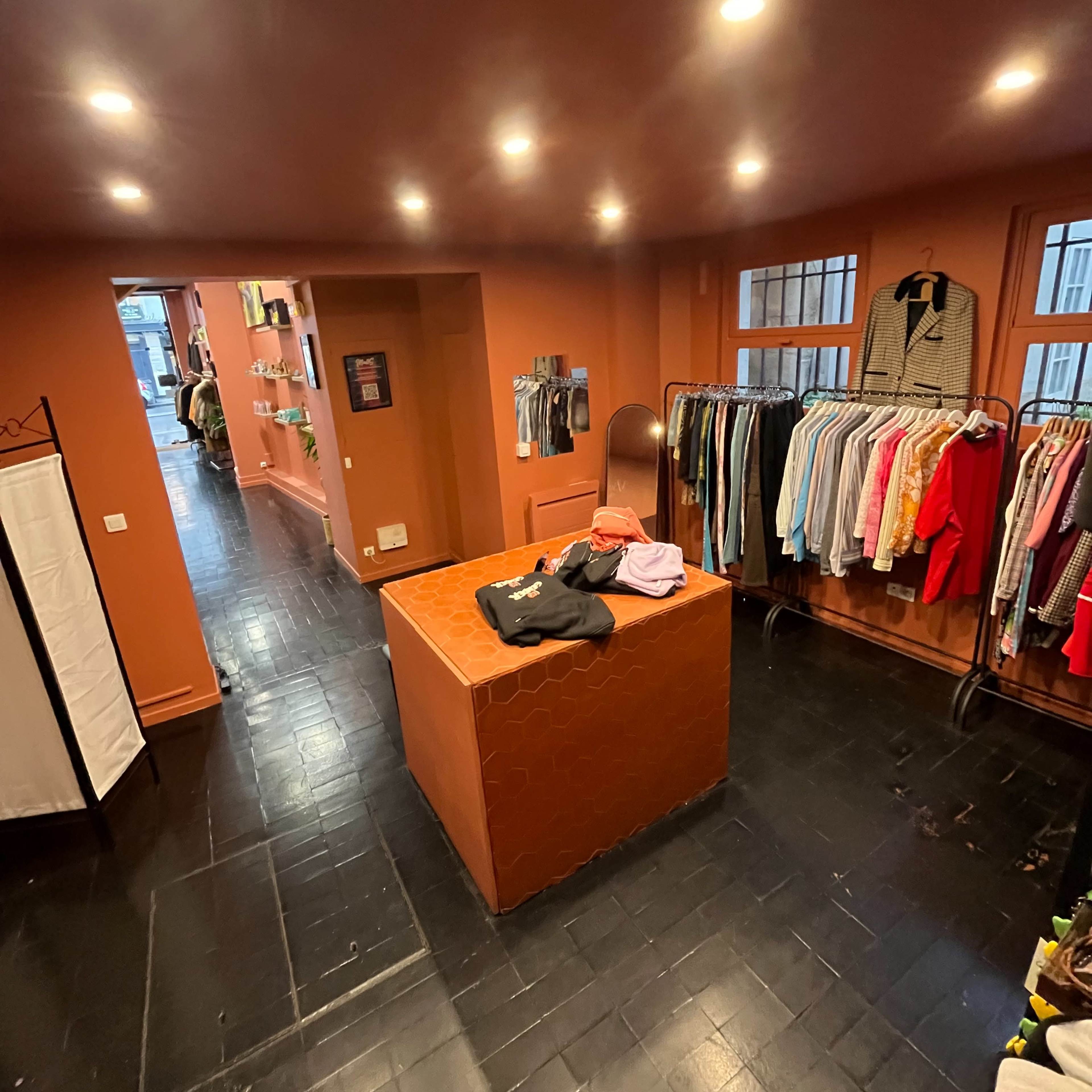 A boutique interior featuring a central display table and clothing racks along the walls, all set against a warm, colored backdrop.
