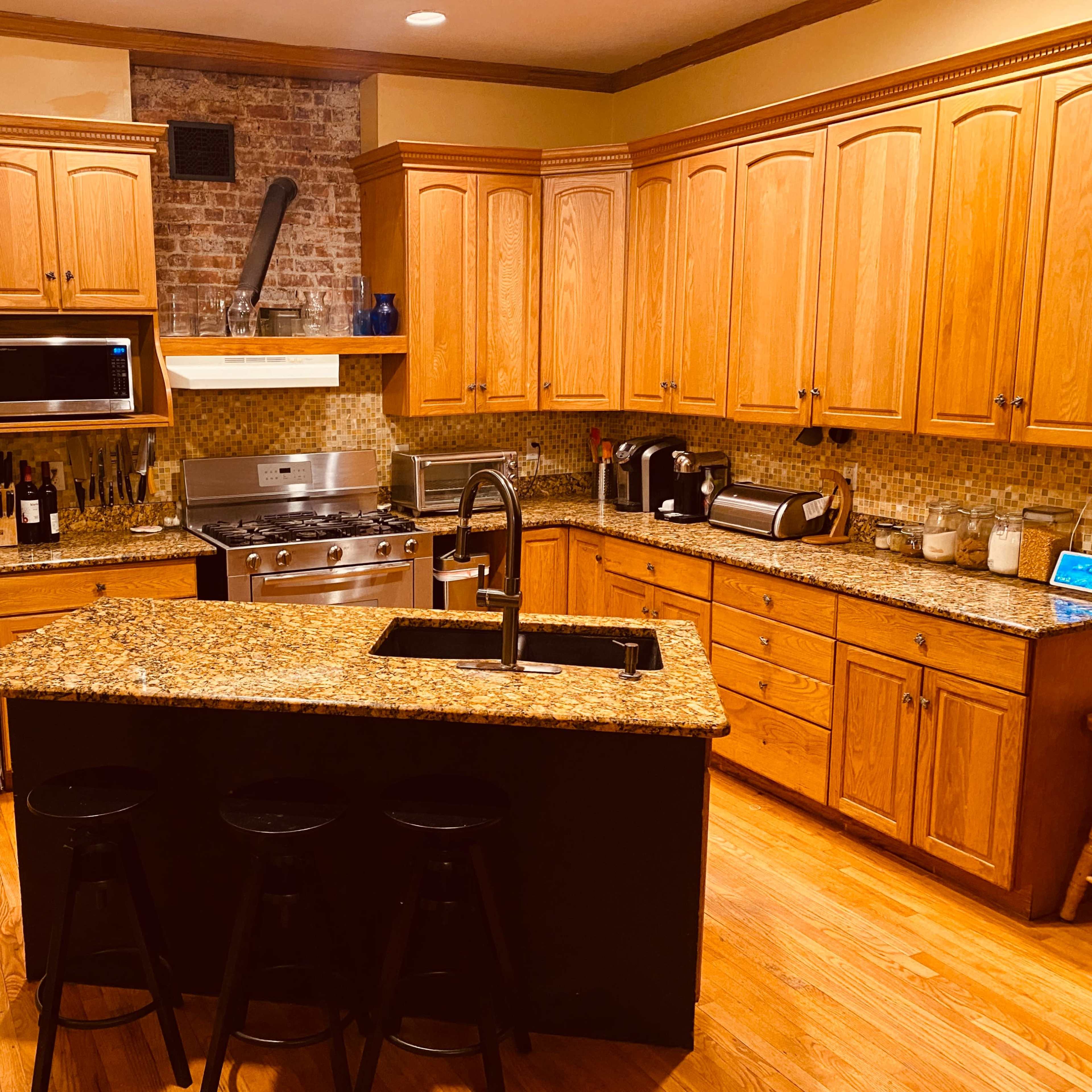 The kitchen features wooden cabinets, a stainless-steel refrigerator, a gas range, and an island with bar stools.