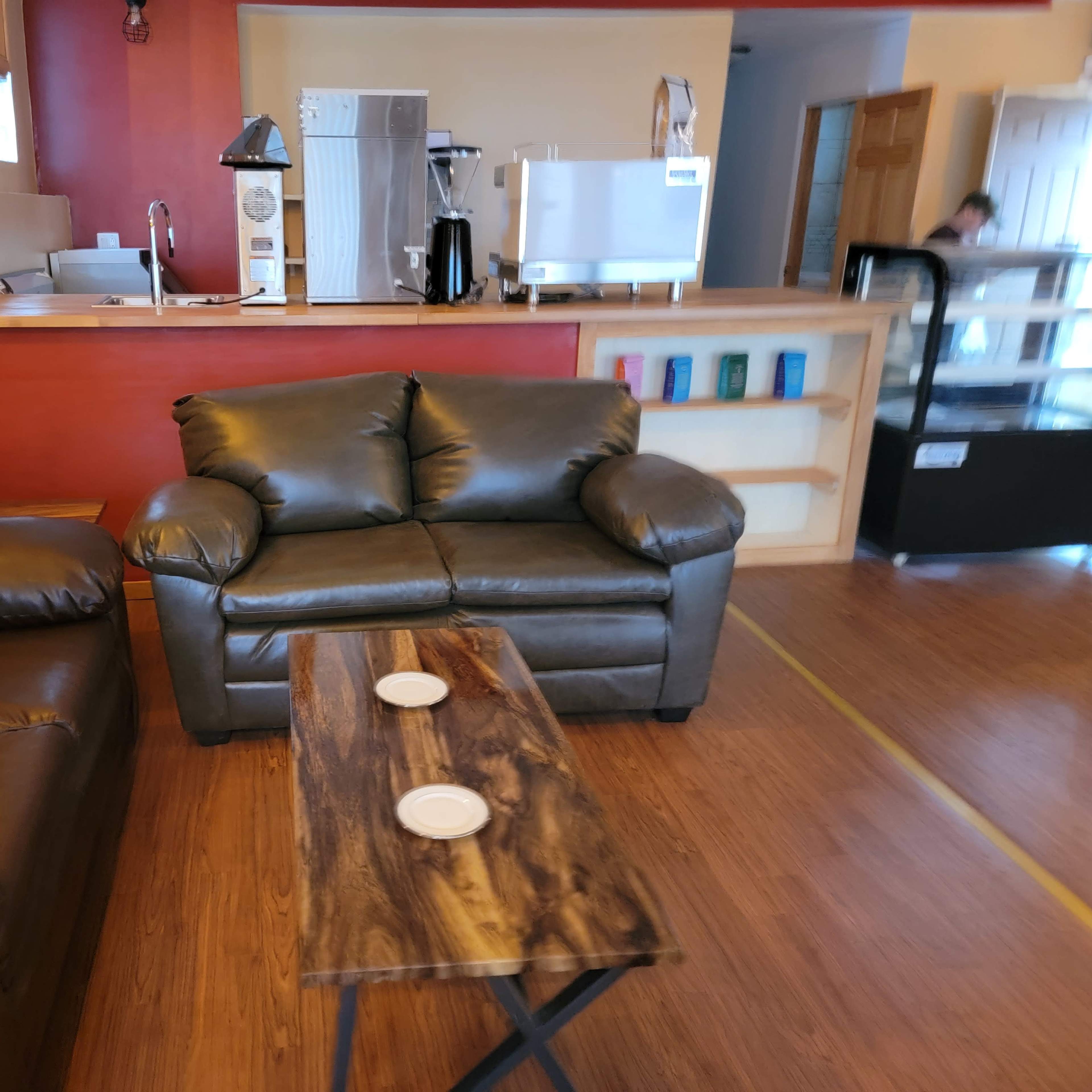 A cozy seating area with two dark leather couches and a wooden coffee table, set in a room with a kitchenette in the background.