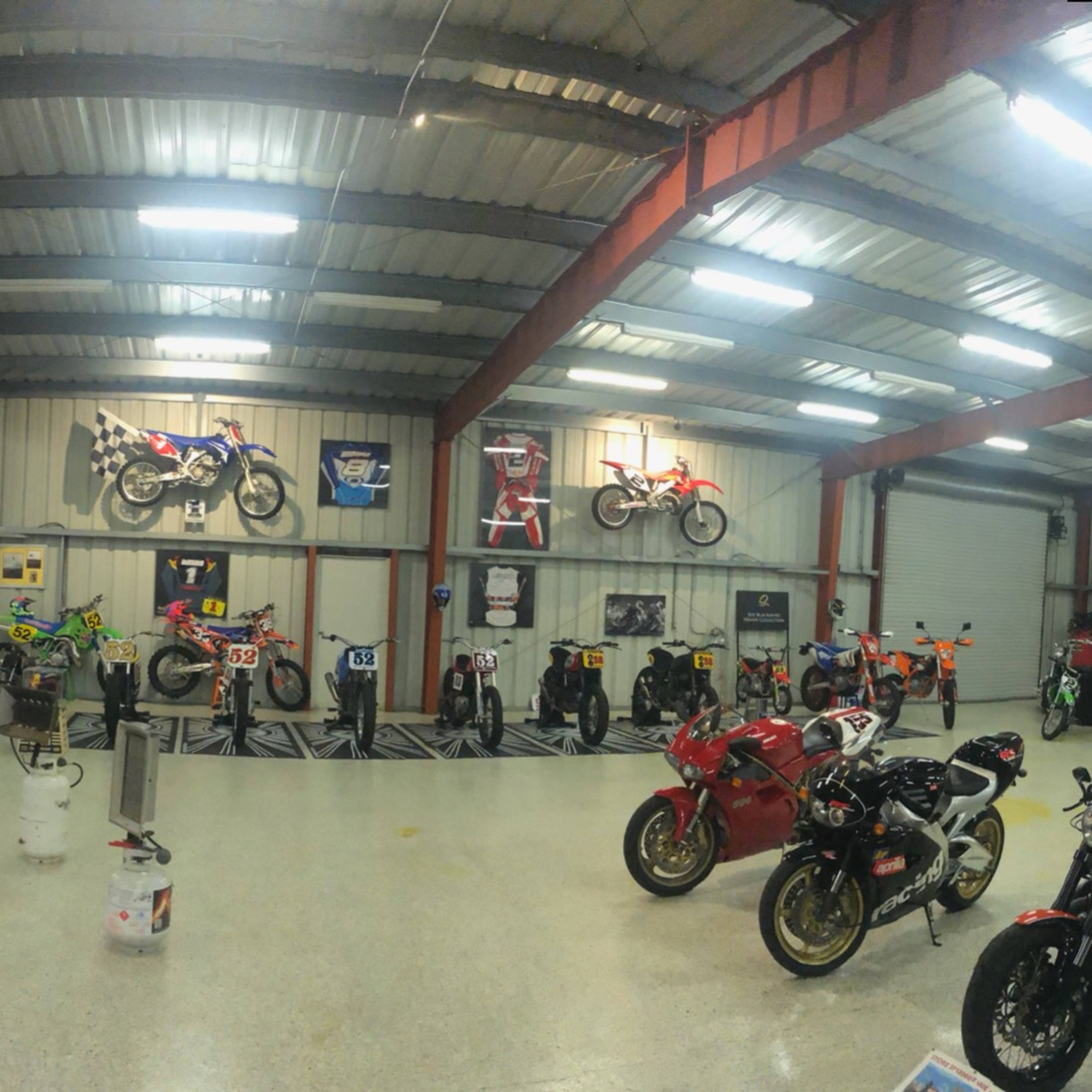 A spacious garage filled with various motorcycles, motorcycle memorabilia, bar stools, and a lounge area.