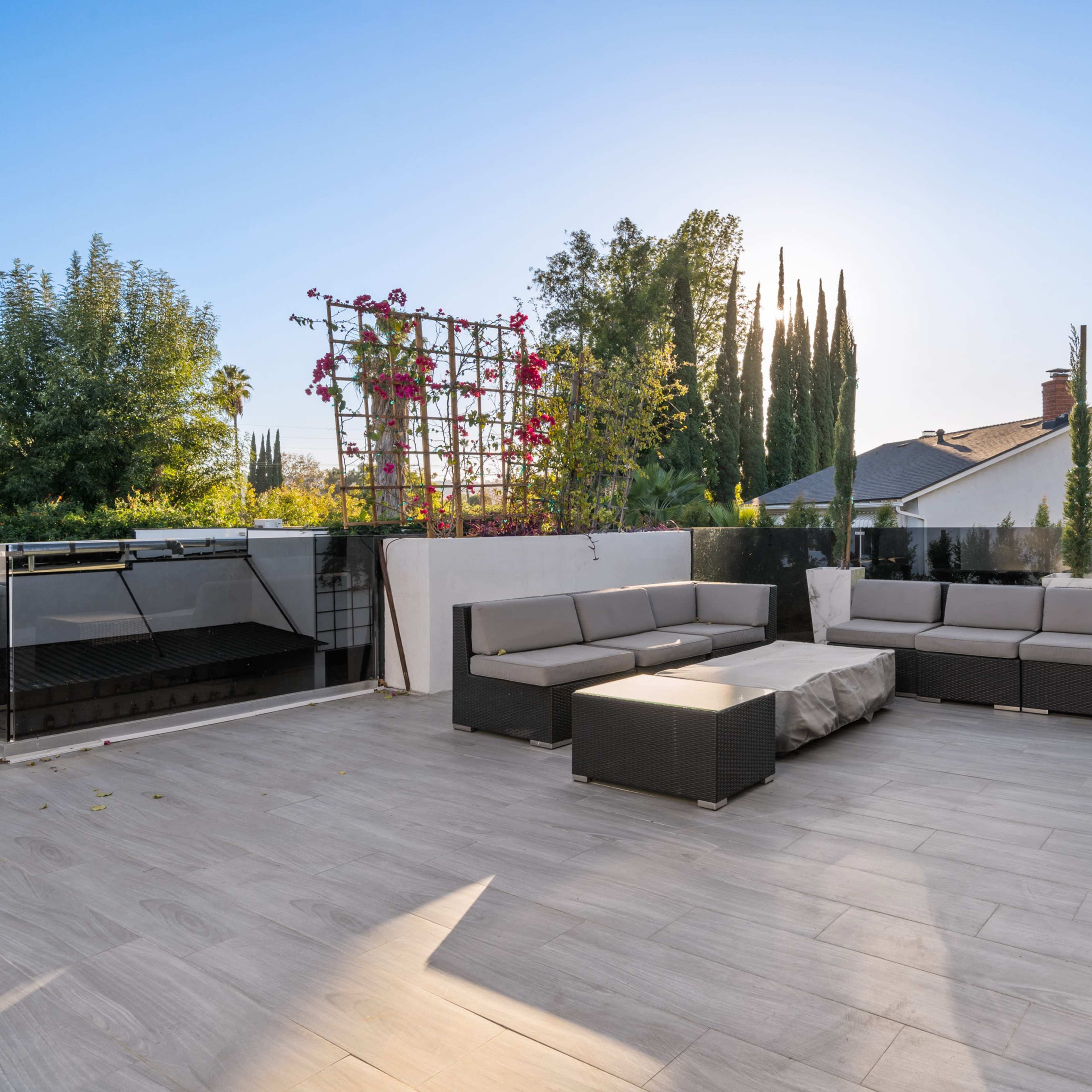 A spacious rooftop terrace with a seating area, a large table, and surrounding greenery under a clear sky.