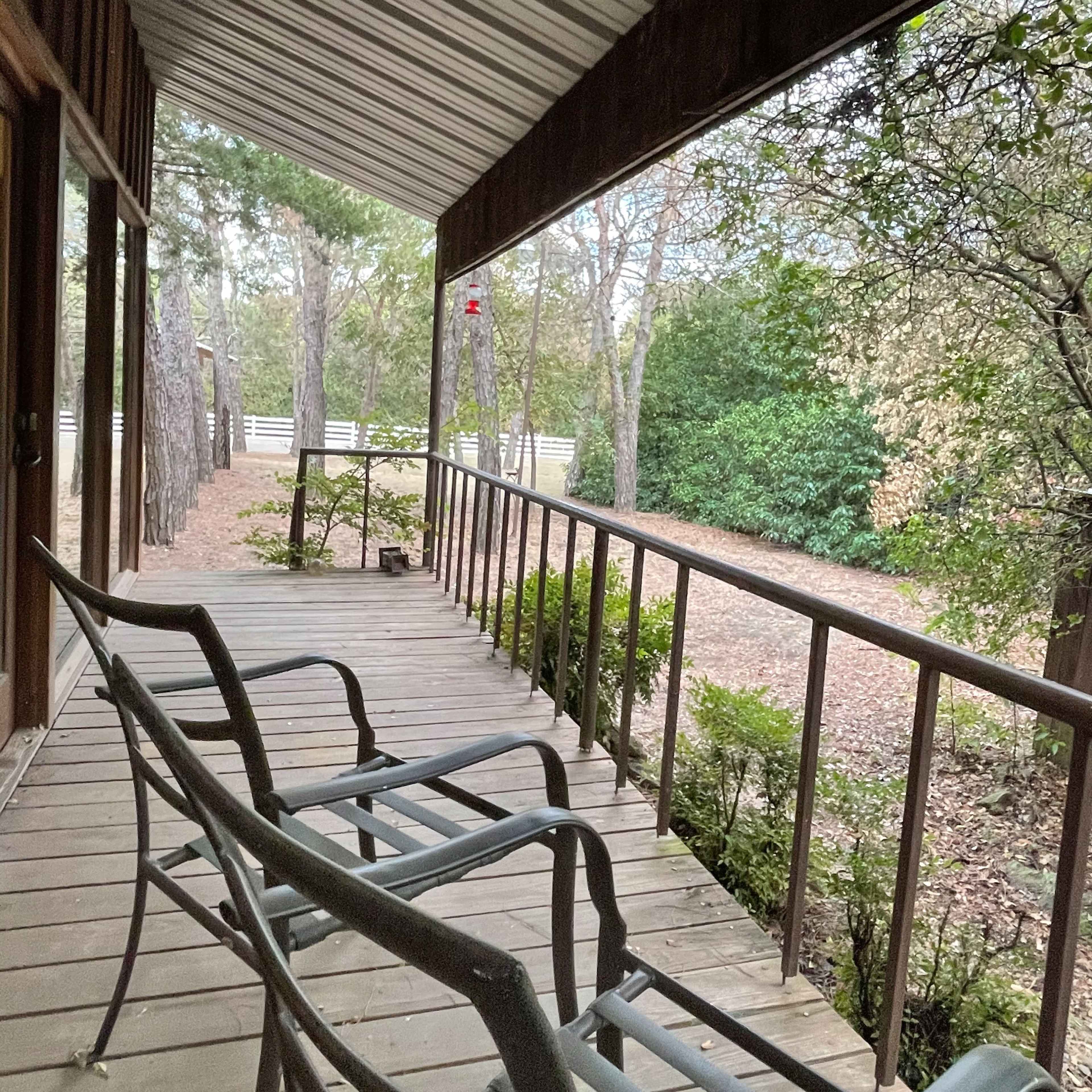 A porch with two metal chairs overlooks a landscape of trees and shrubs.