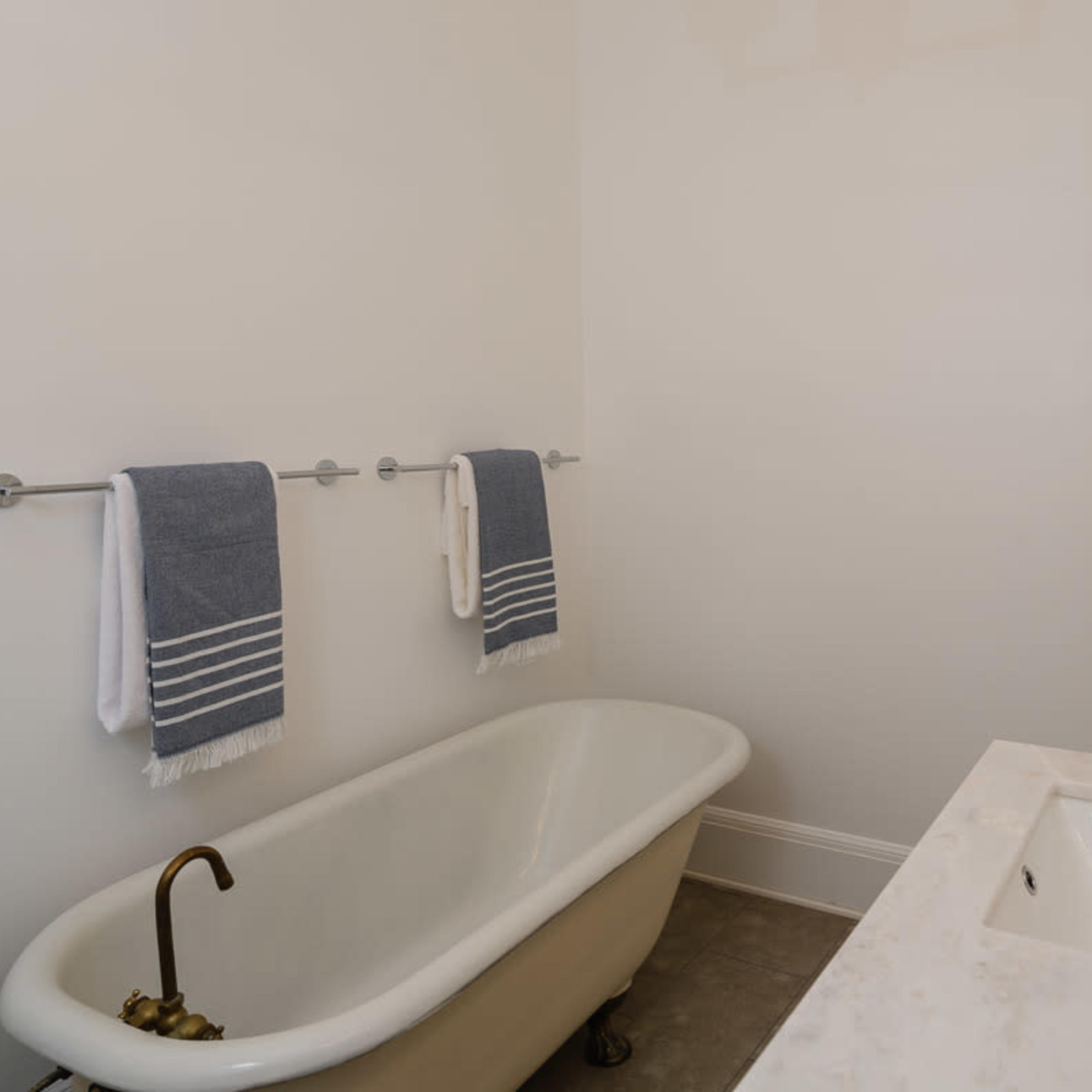 A minimalist bathroom featuring a freestanding white bathtub, a marble countertop with a sink, and two towels hanging on chrome racks.