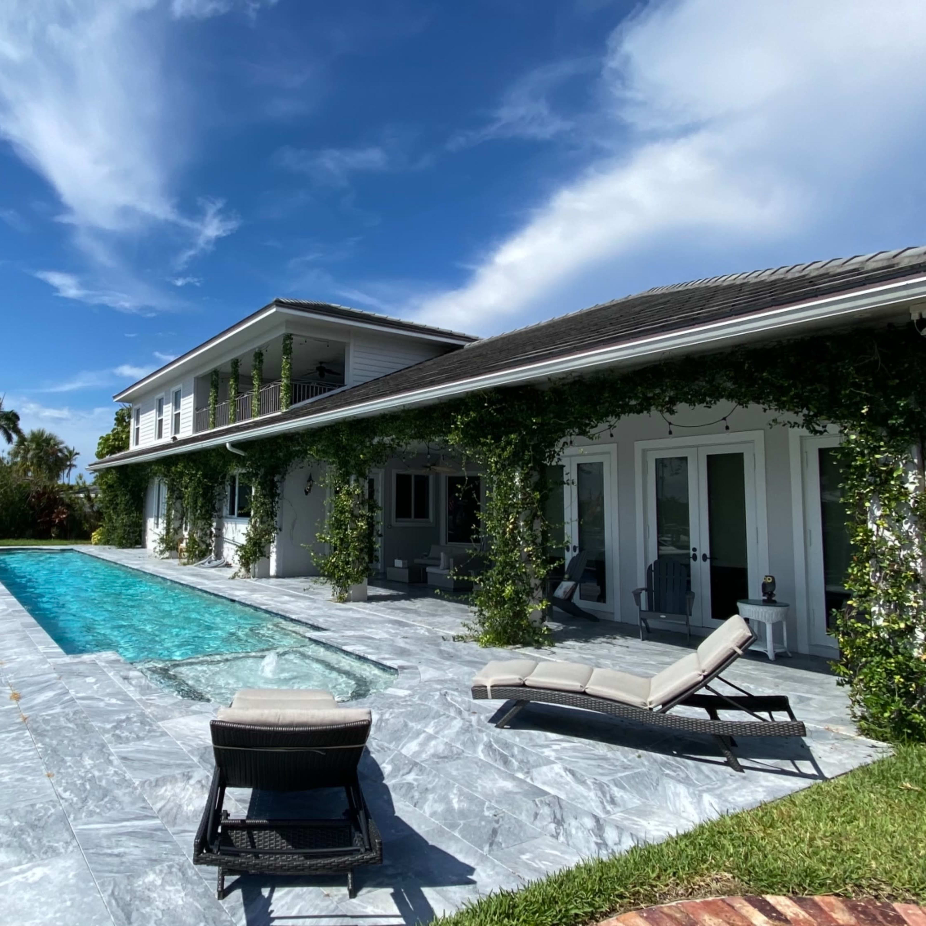 A modern house with a swimming pool and lounge chairs, situated beside a marina with boats in the background.