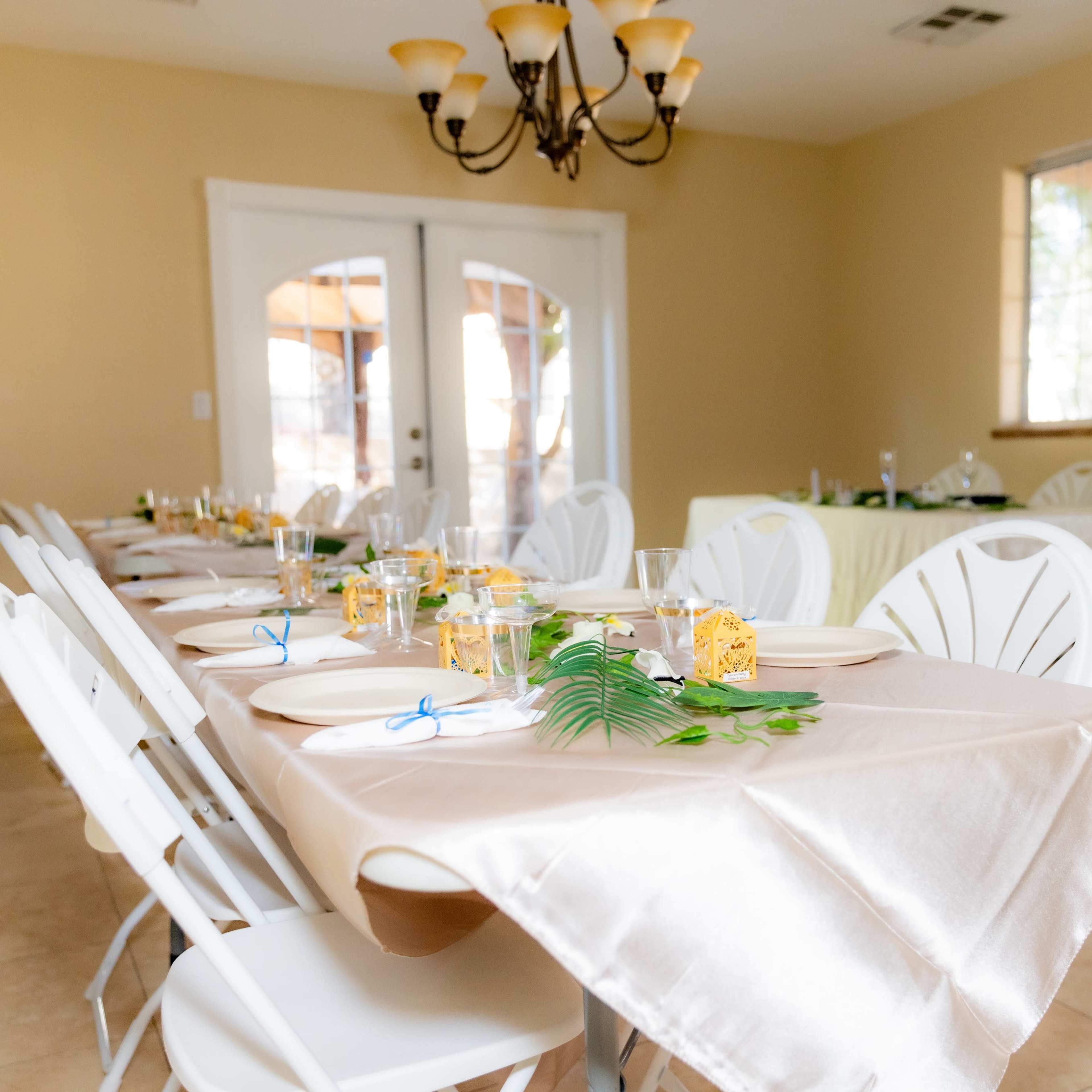 A dining area set with multiple tables draped in light-colored tablecloths, each featuring plates, glasses, and decorative elements.