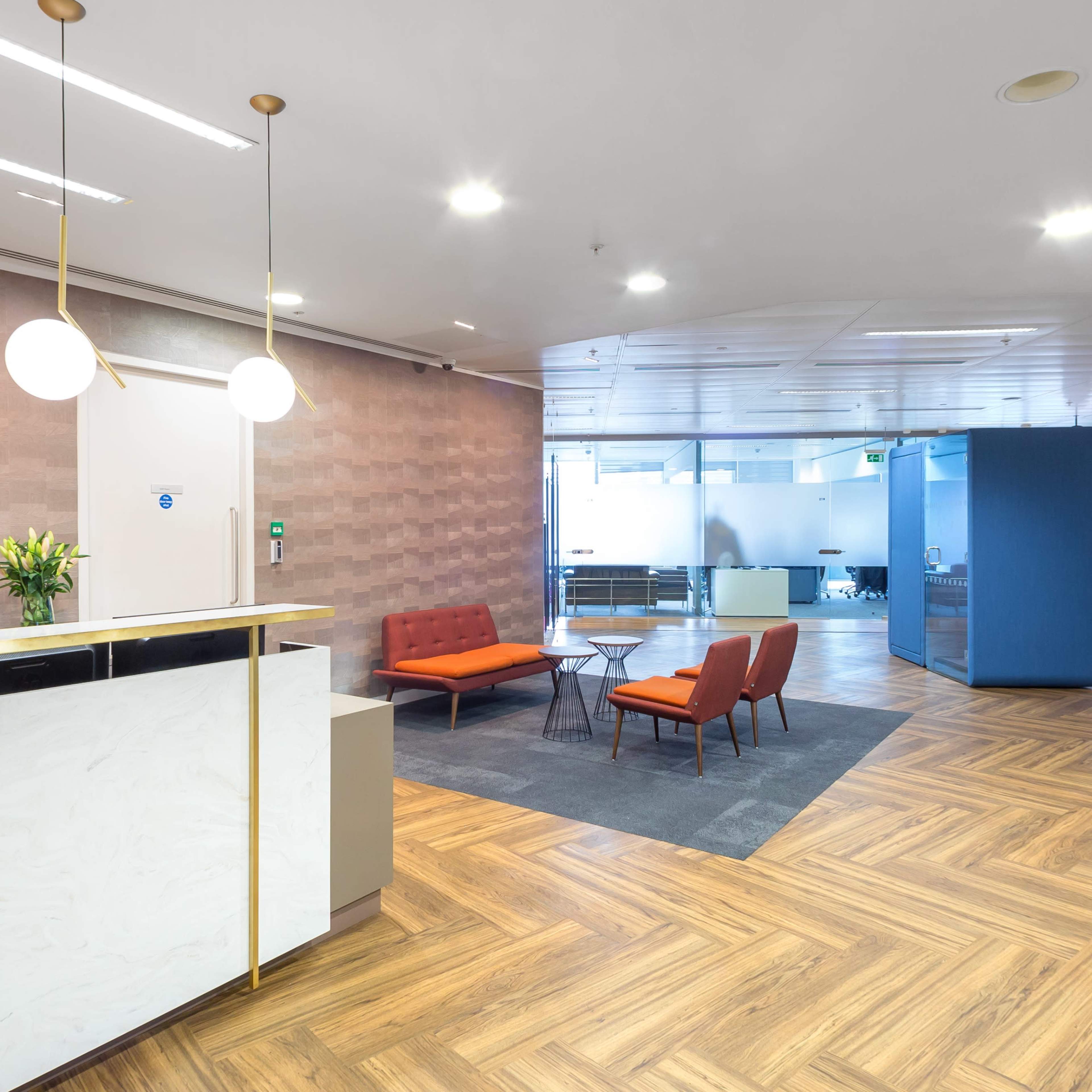 A modern office reception area with a front desk, seating arrangements, and a digital display.