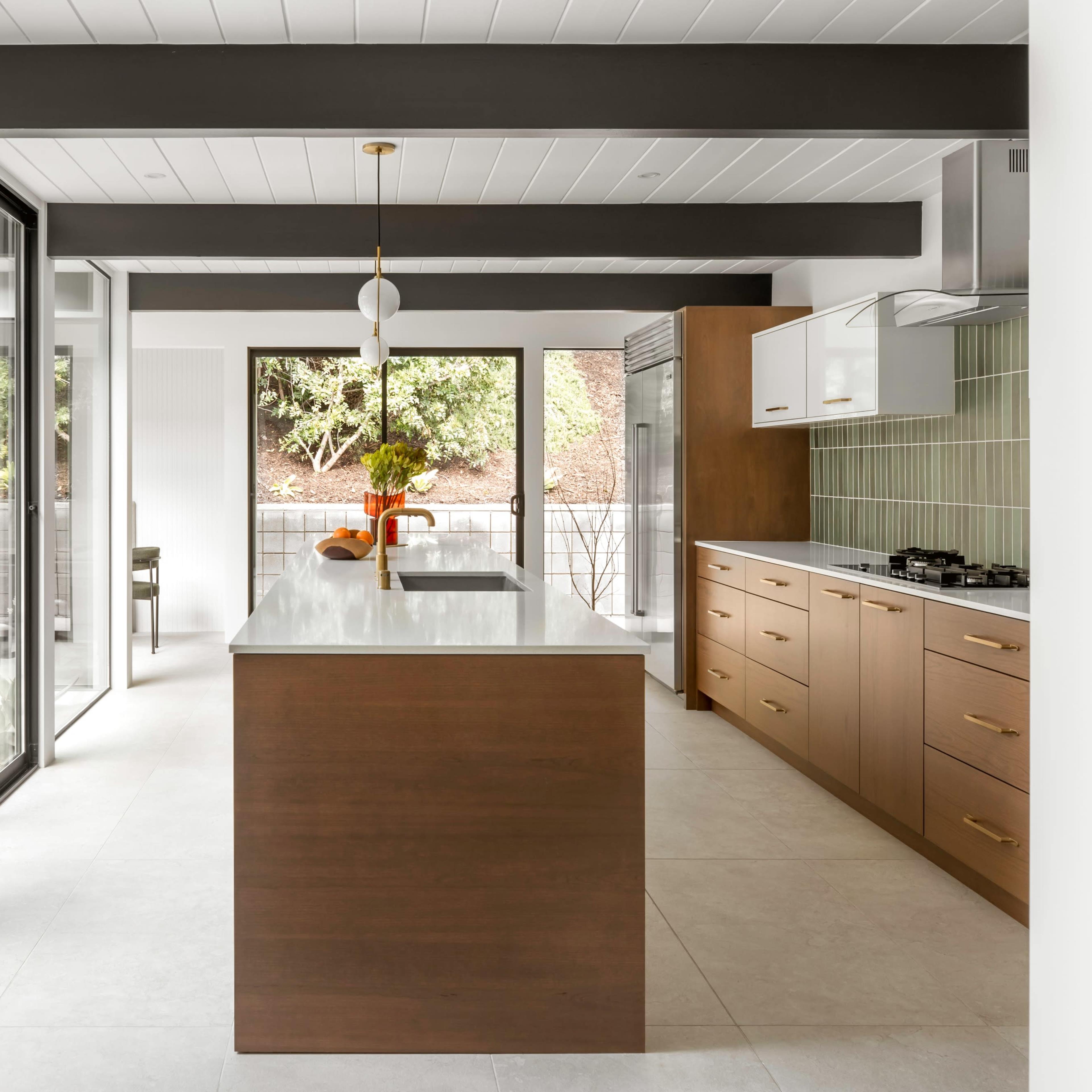 A modern kitchen with a central island, wooden cabinetry, and large glass doors opening to an outdoor space.