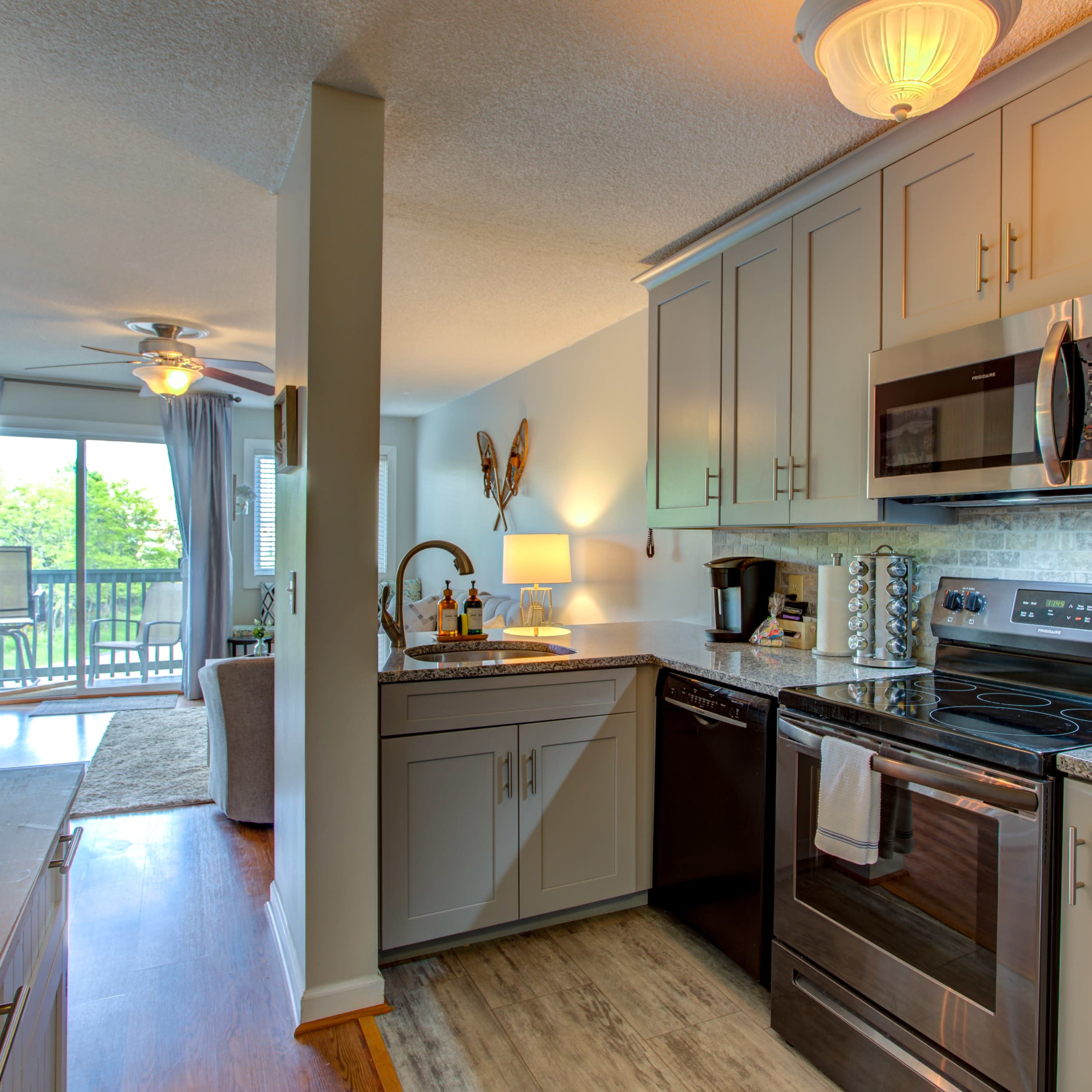 A modern kitchen features stainless steel appliances and a view of a balcony through an open living area.