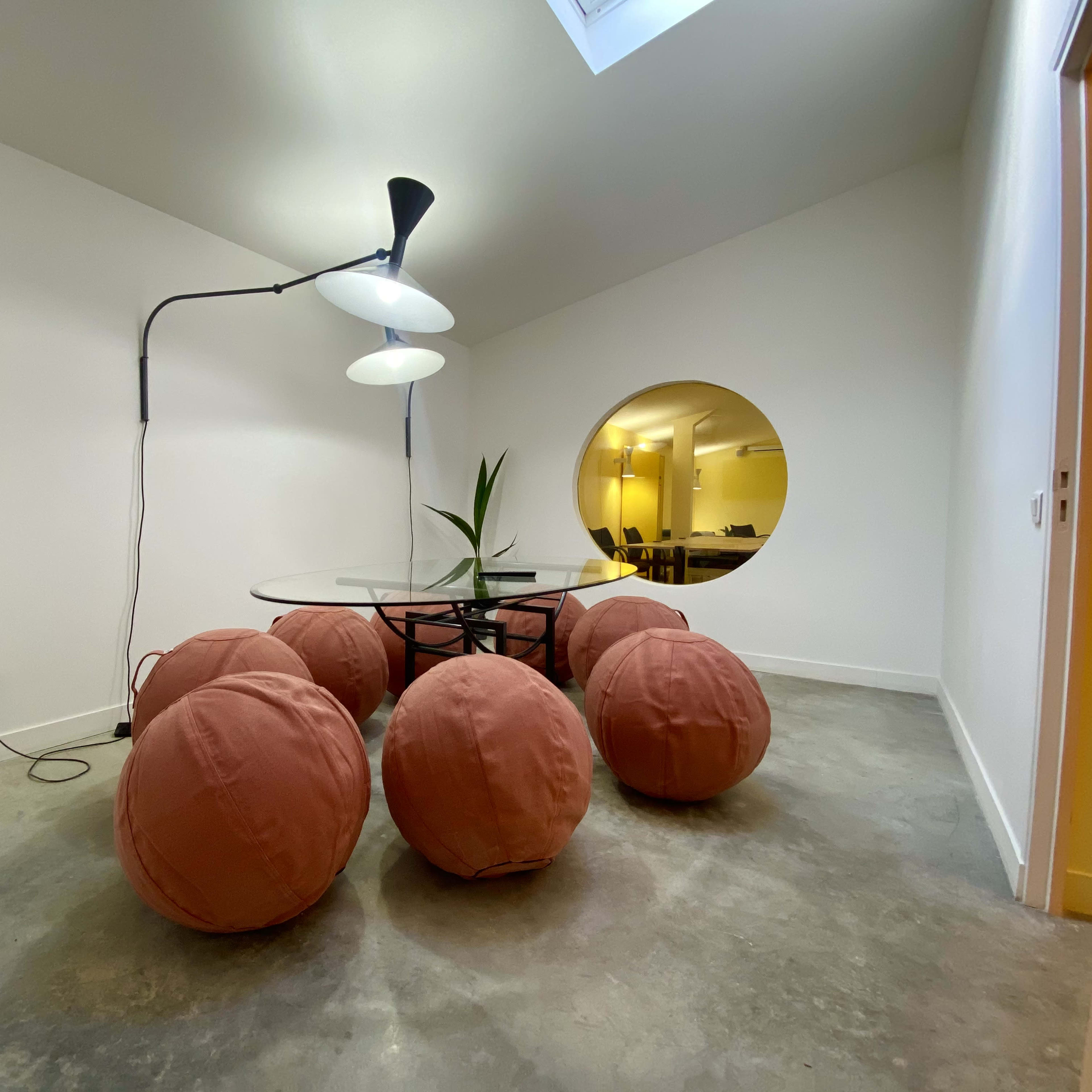 A minimalistic room with a circular mirror, a glass table, and several large, round, orange cushions arranged around it.