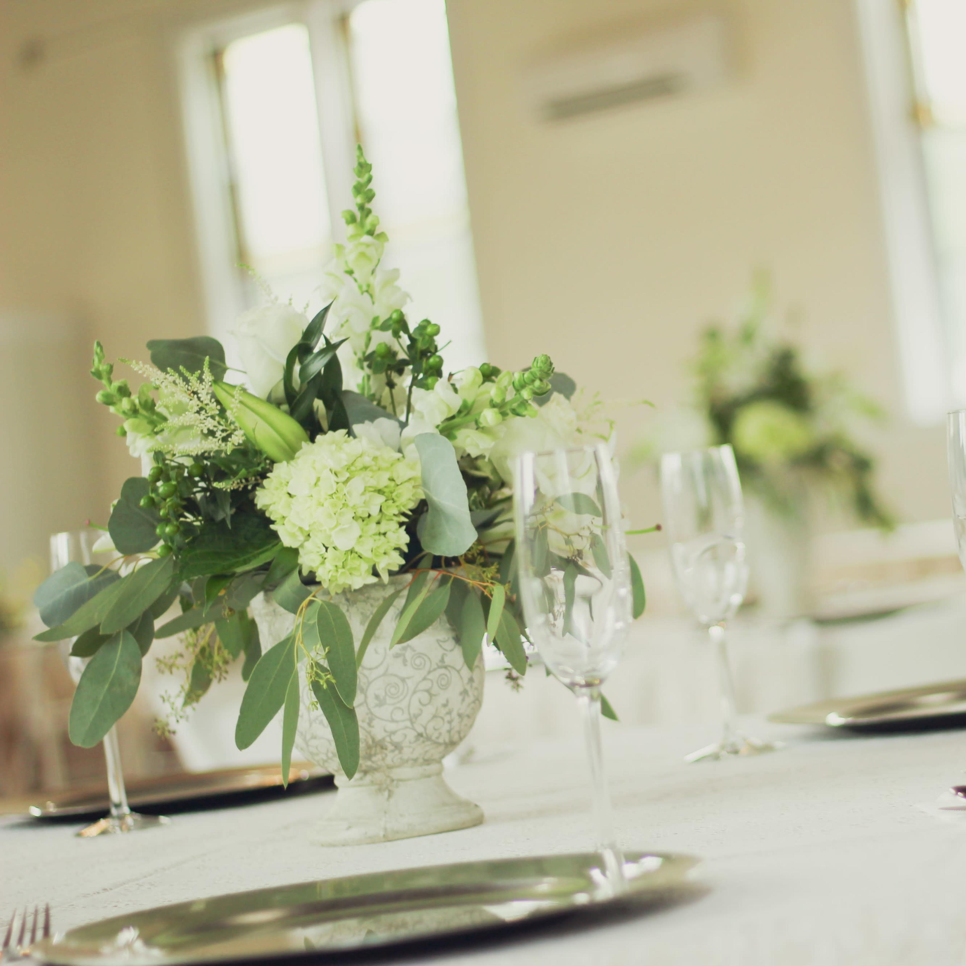 A decorated dining table with a floral arrangement in a vase and set with plates and champagne glasses.