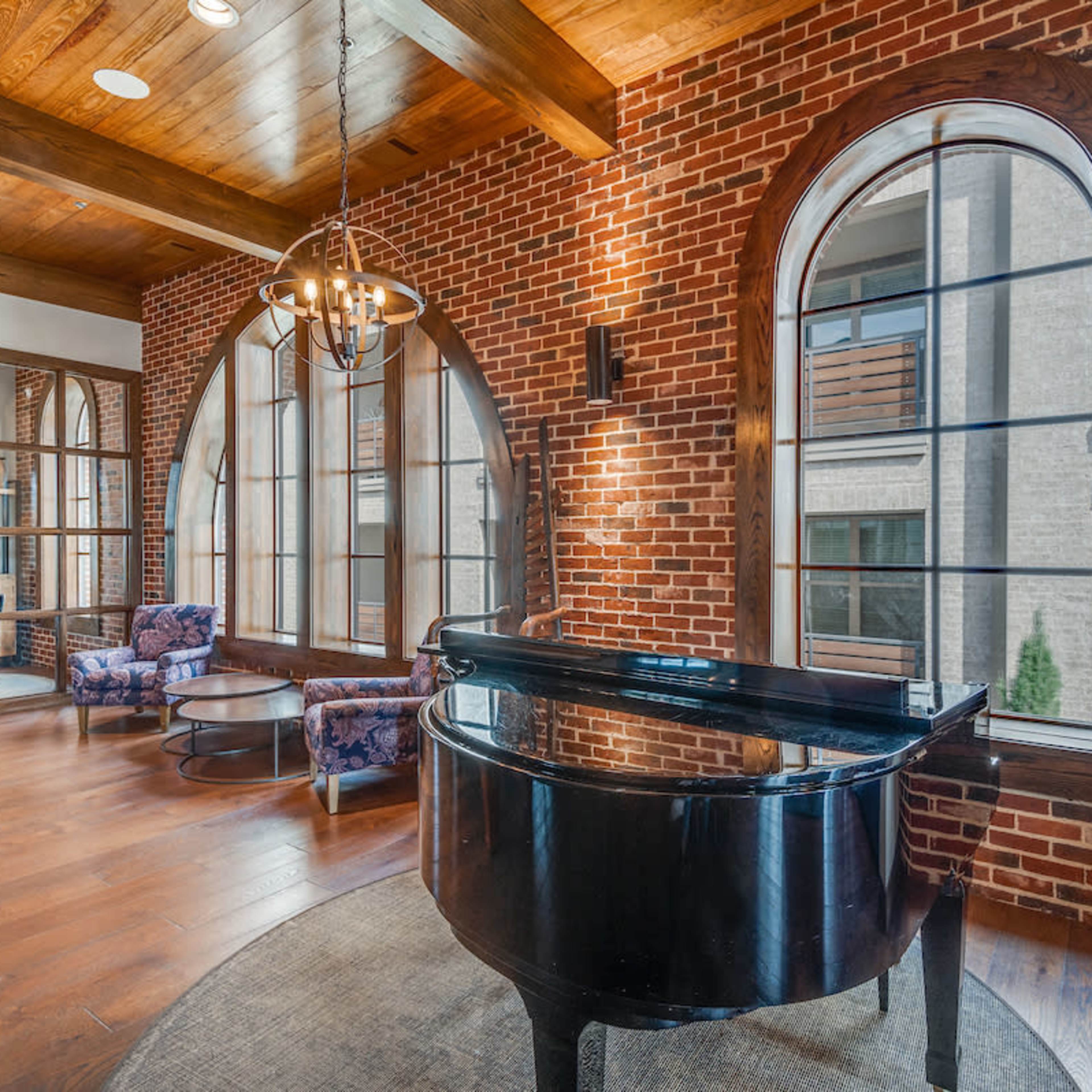A room with exposed brick walls, wood beams, and a grand piano positioned in front of large arched windows.