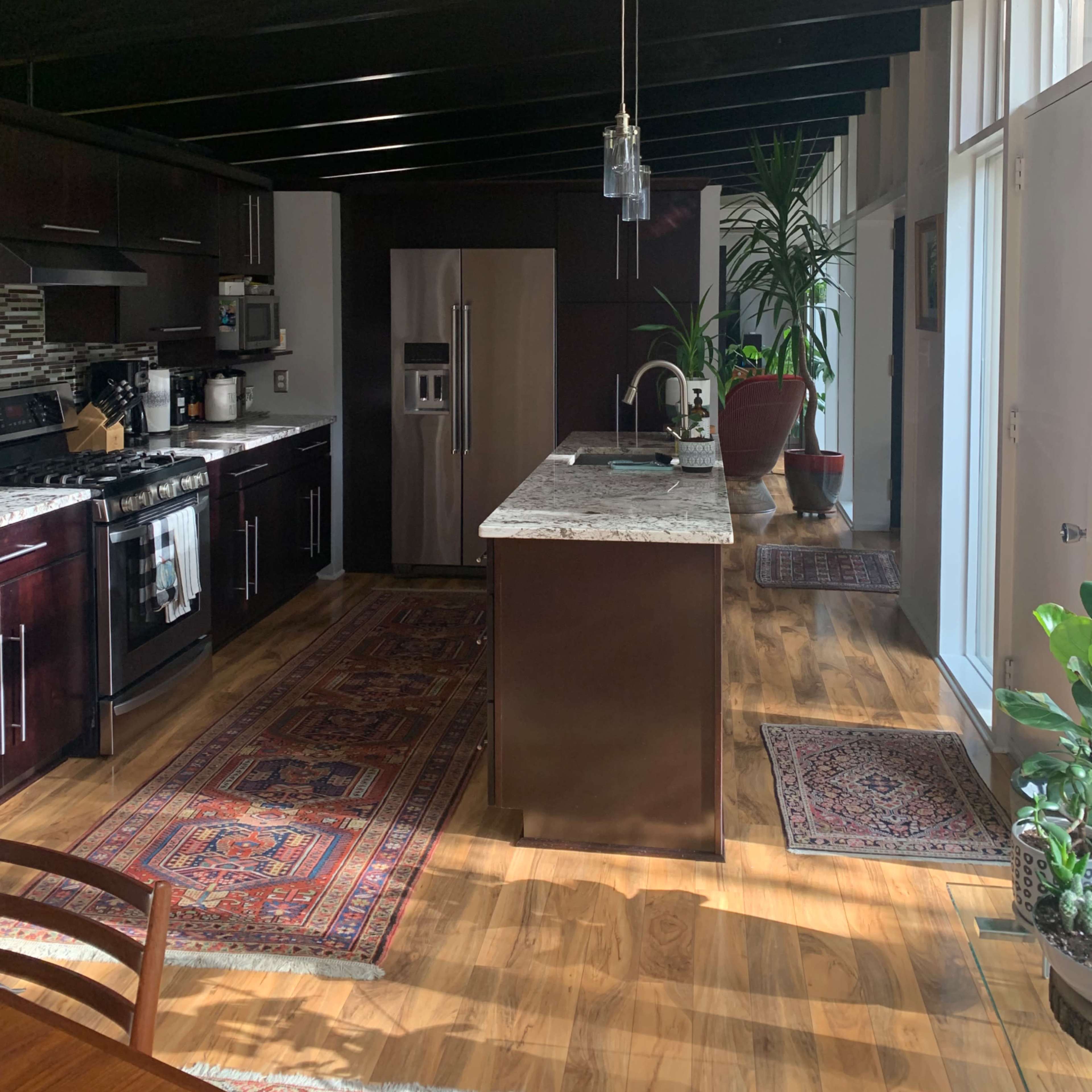 A modern kitchen with dark wood cabinets, a central island topped with granite, and large windows allowing natural light to enter the space.