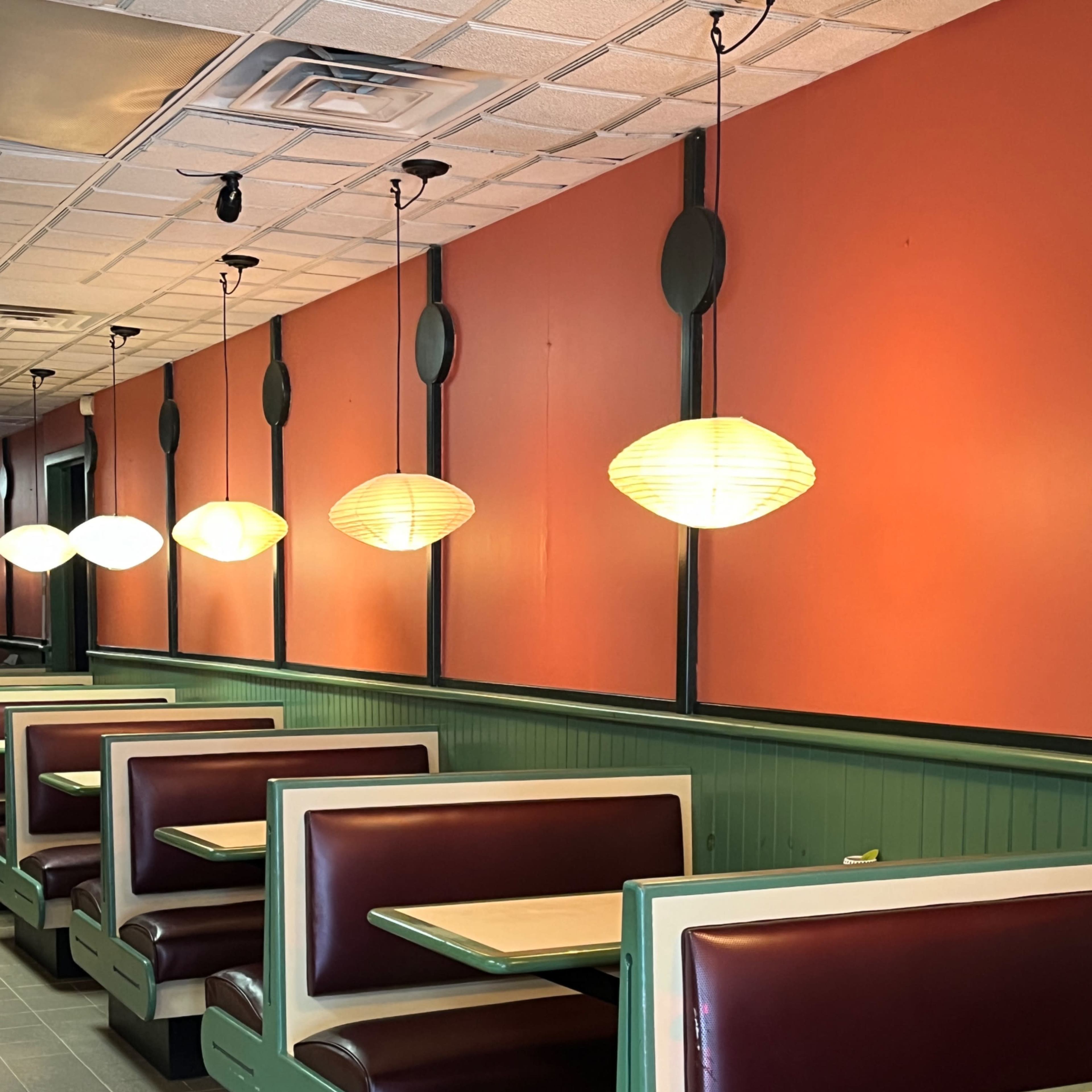 A row of brown-and-cream booths in a diner with orange walls and hanging pendant lights.