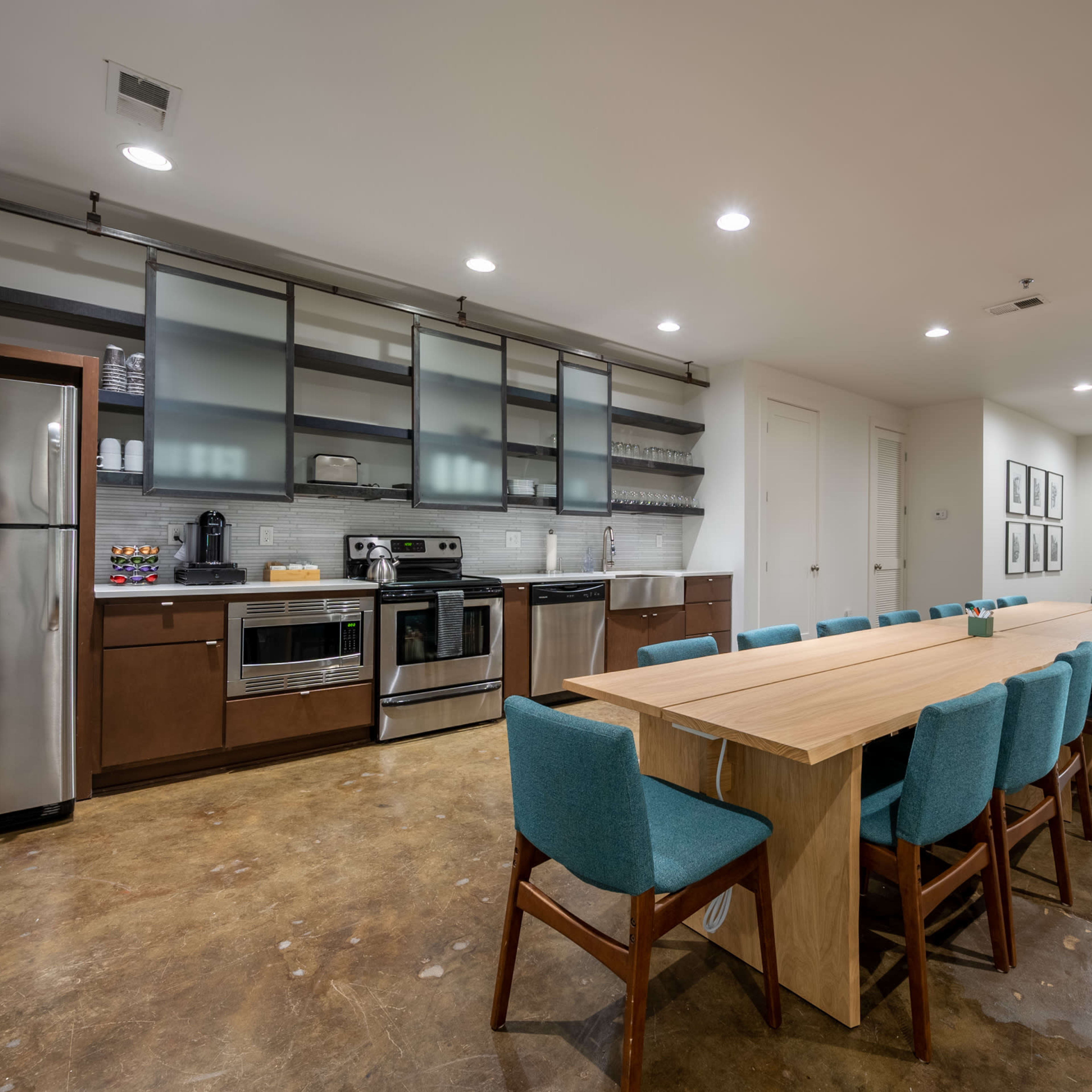 A modern kitchen and dining area featuring stainless steel appliances, a long wooden table with teal chairs, and a minimalist design.